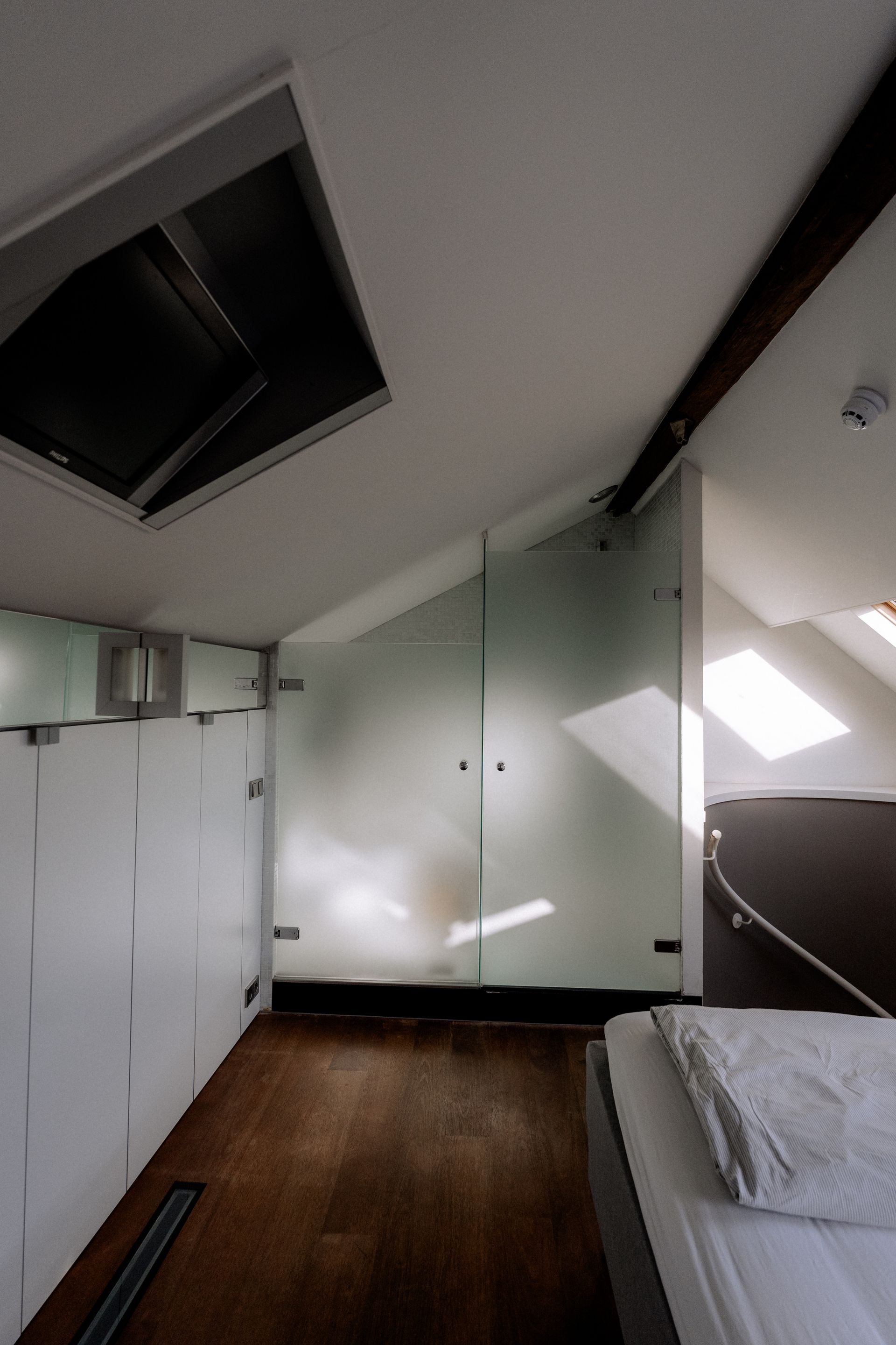 Slaapkamer met een schuin plafond, glazen wand en deur, en een dakraam. Op de voorgrond staat een bed.