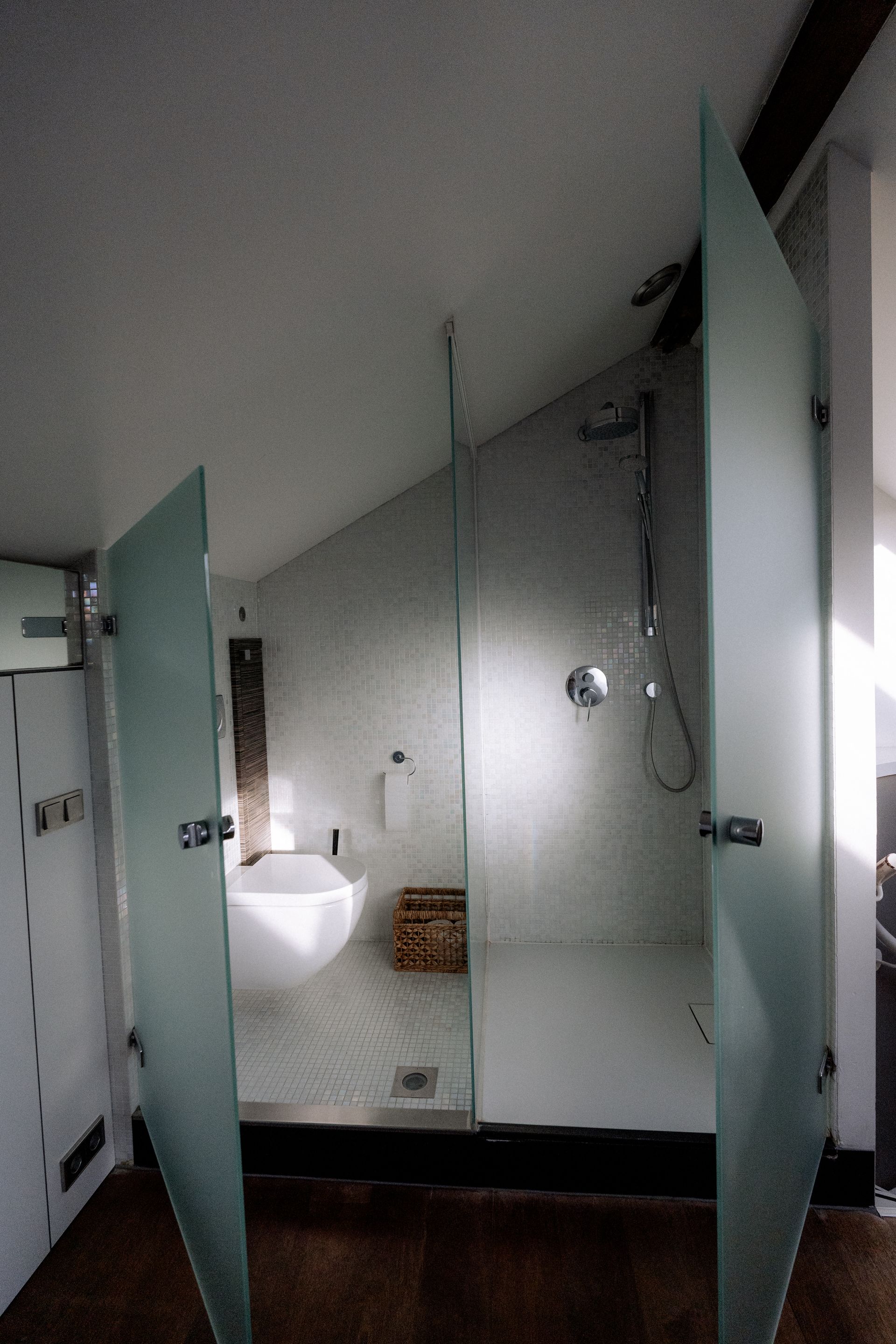 Moderne badkamer met douchedeuren van matglas, witte armaturen en een schuin plafond.