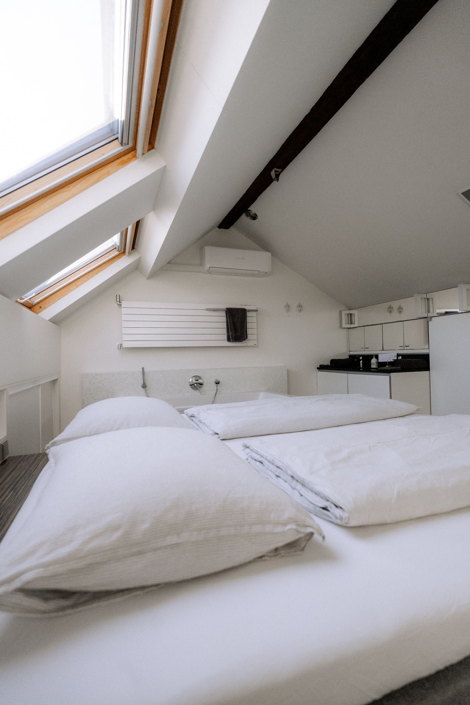Slaapkamer met wit beddengoed, dakraam en een kleine keukenhoek.