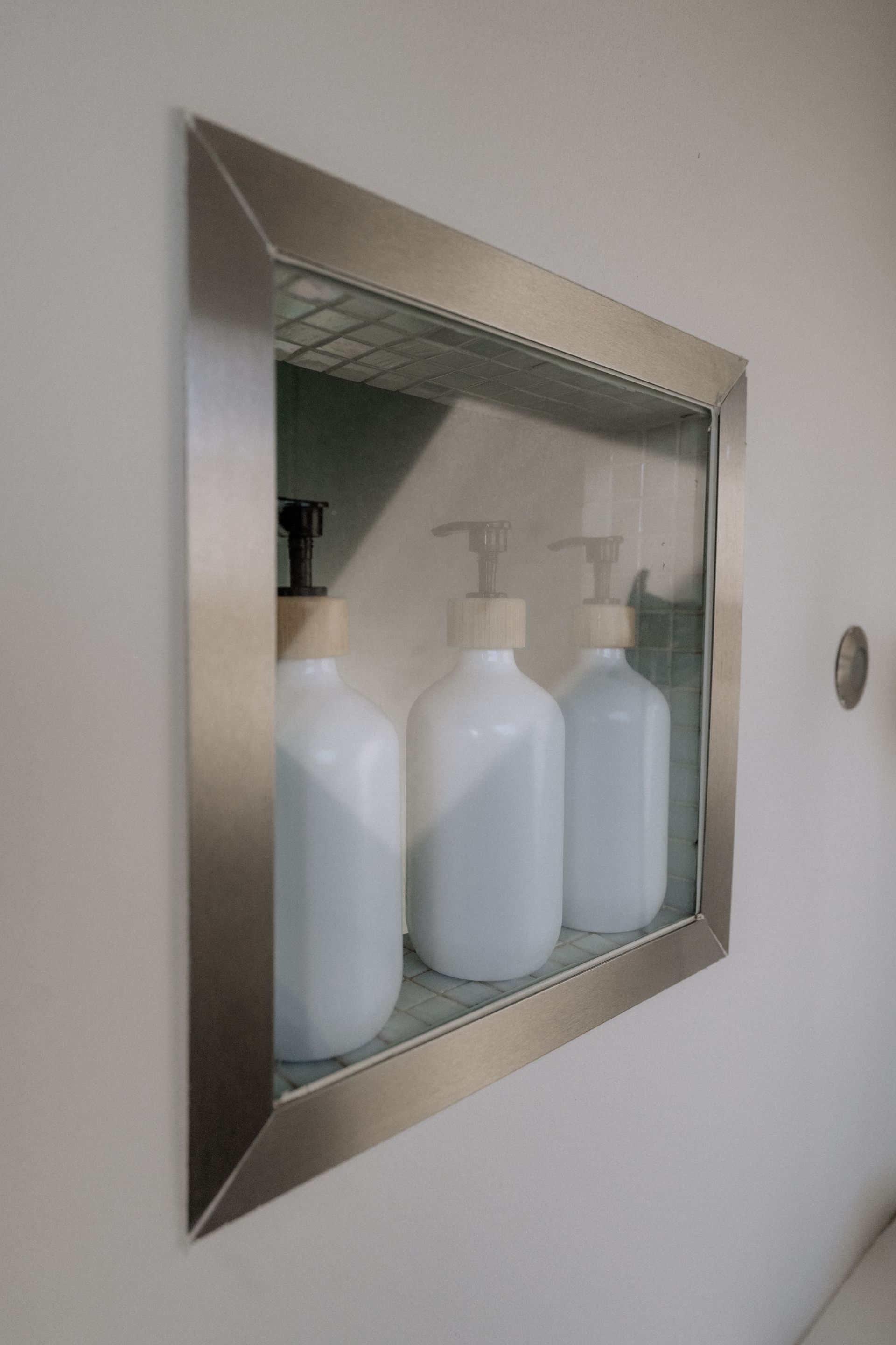 Inbouwdouchenis met drie witte flessen, metalen frame en accenten op een witte muur.