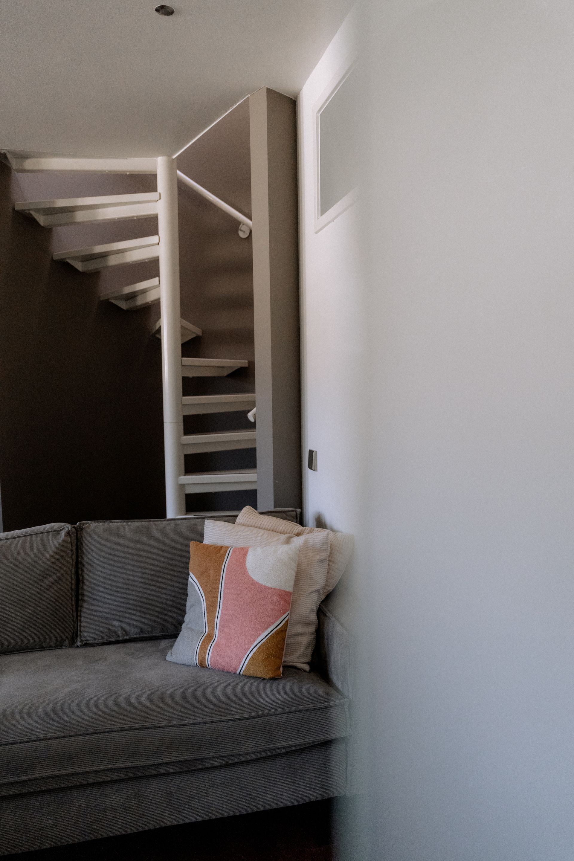 Grijze bank met sierkussens bij een wenteltrap in een kamer.