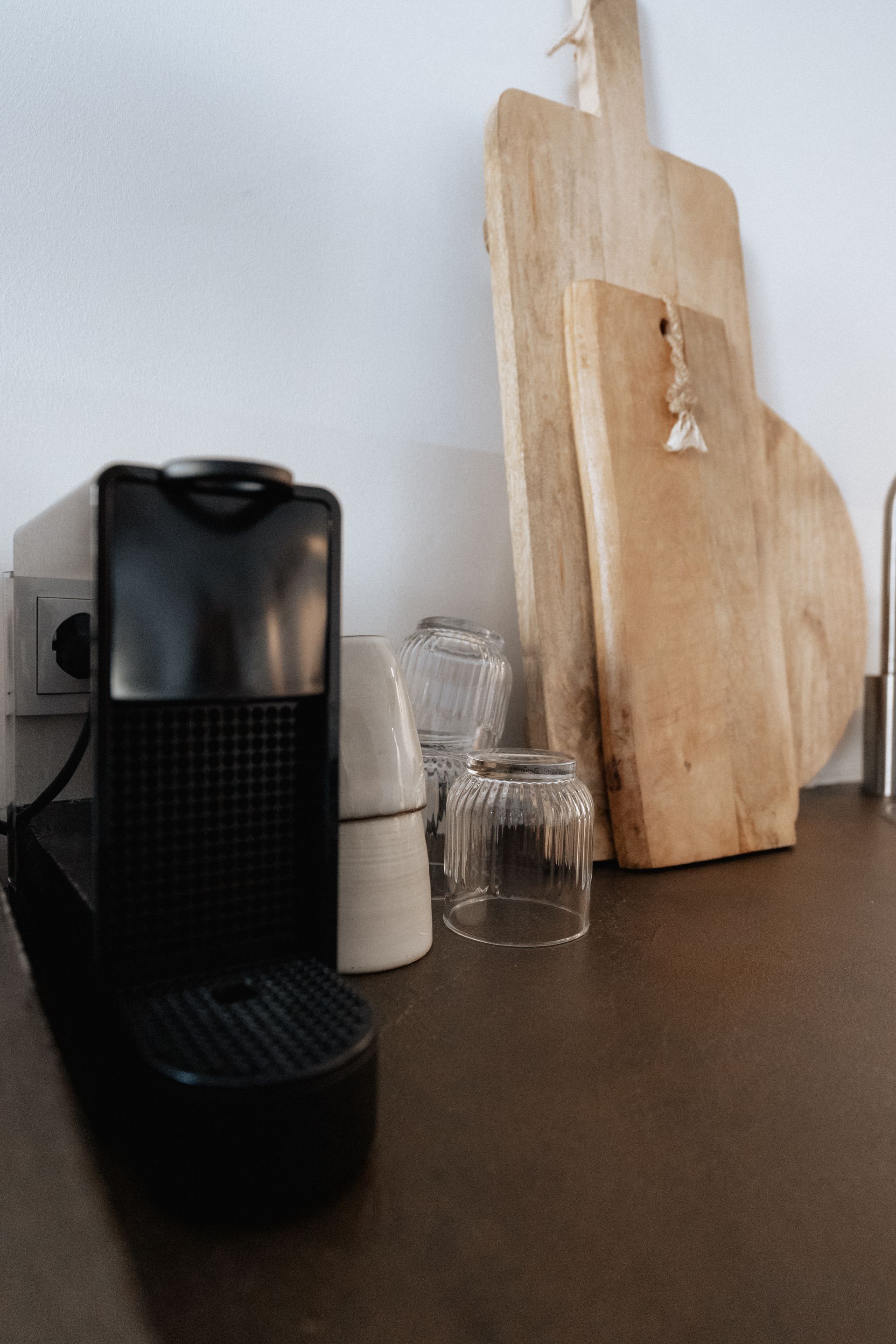 Een zwart koffiezetapparaat, snijplanken en kopjes staan ​​op een donker aanrecht in een keuken.