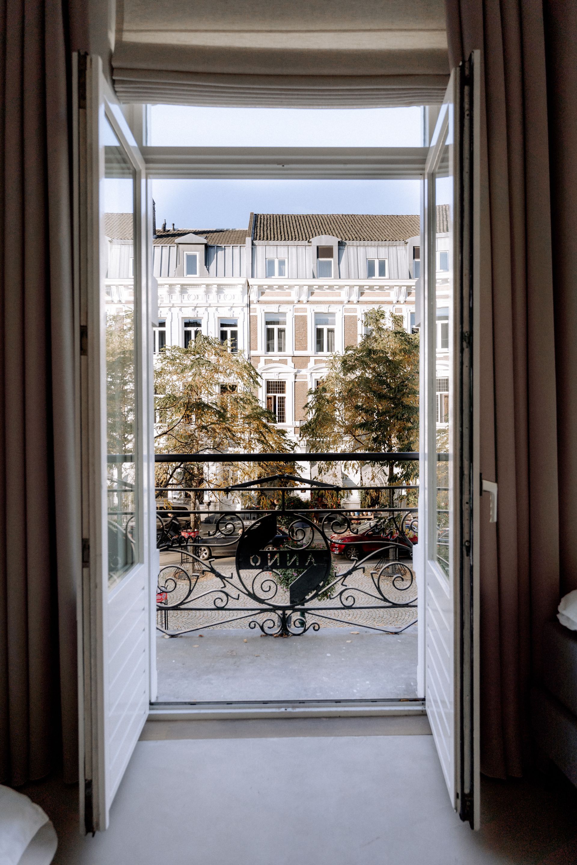Openstaande witte deuren onthullen een balkon met uitzicht op een stadsstraat met gebouwen en bomen.