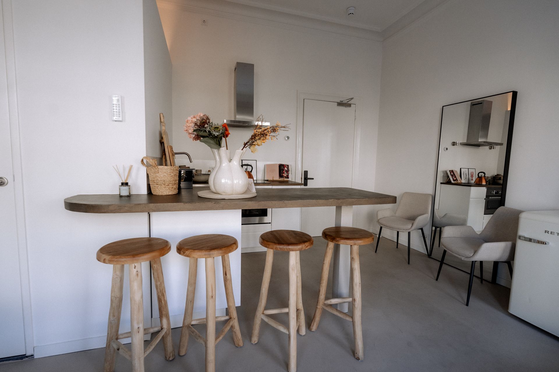 Een moderne keuken met een houten ontbijtbar, barkrukken en witte muren. Inclusief een minikoelkast en stoelen.