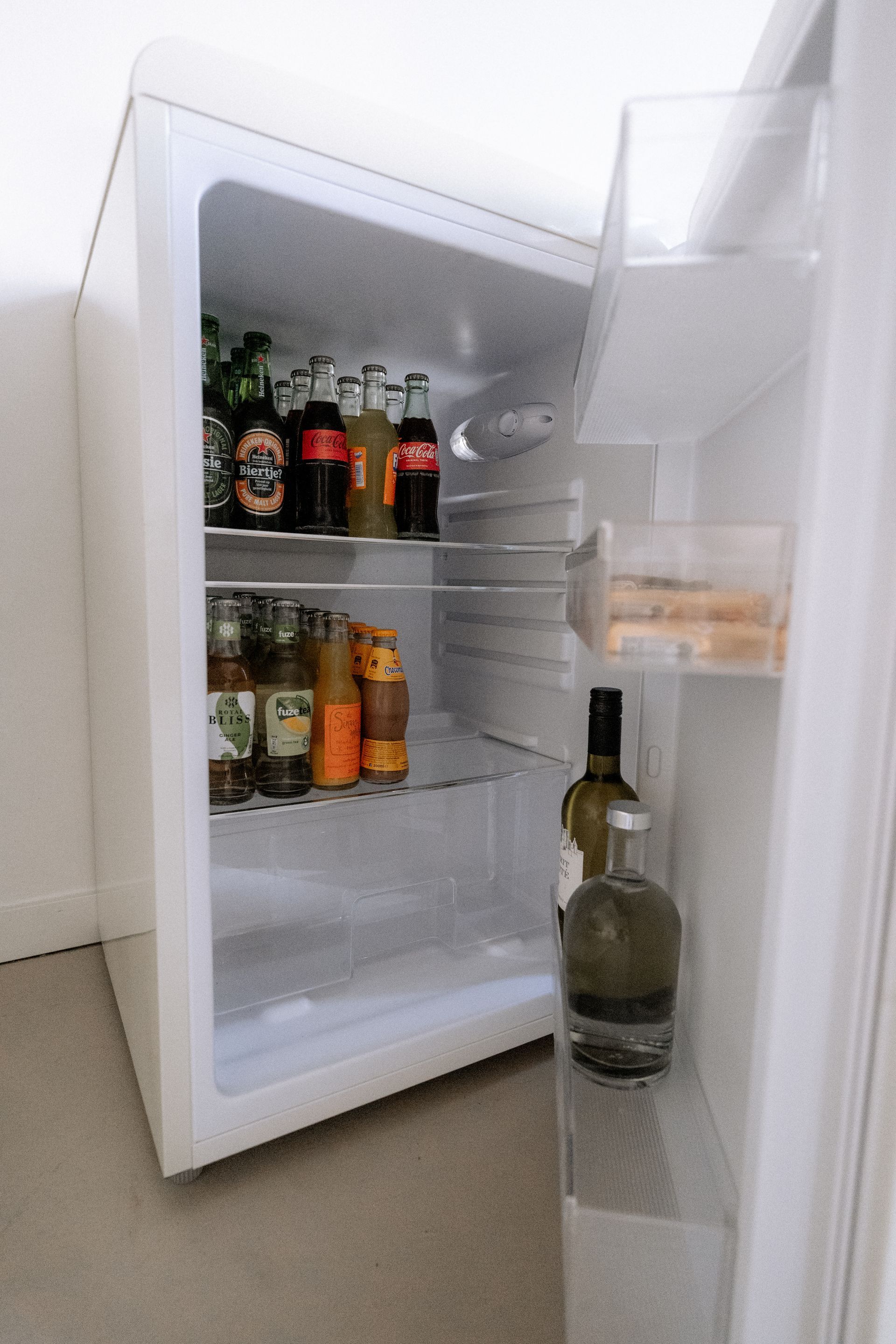 Kleine, open koelkast gevuld met diverse dranken in flessen. Witte binnenkant.