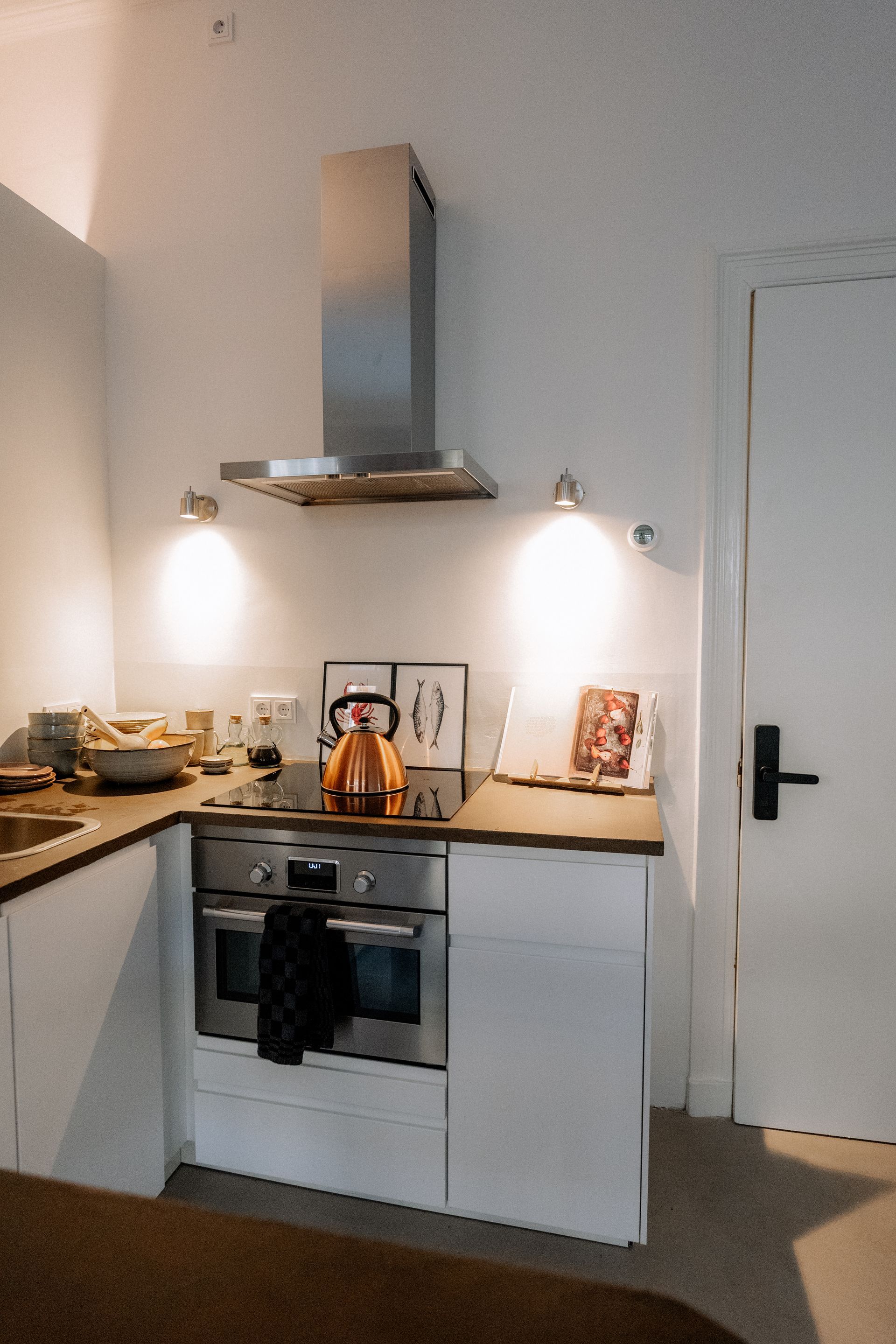 Kleine, moderne keuken met witte kastjes, roestvrijstalen apparaten en een kookboek.