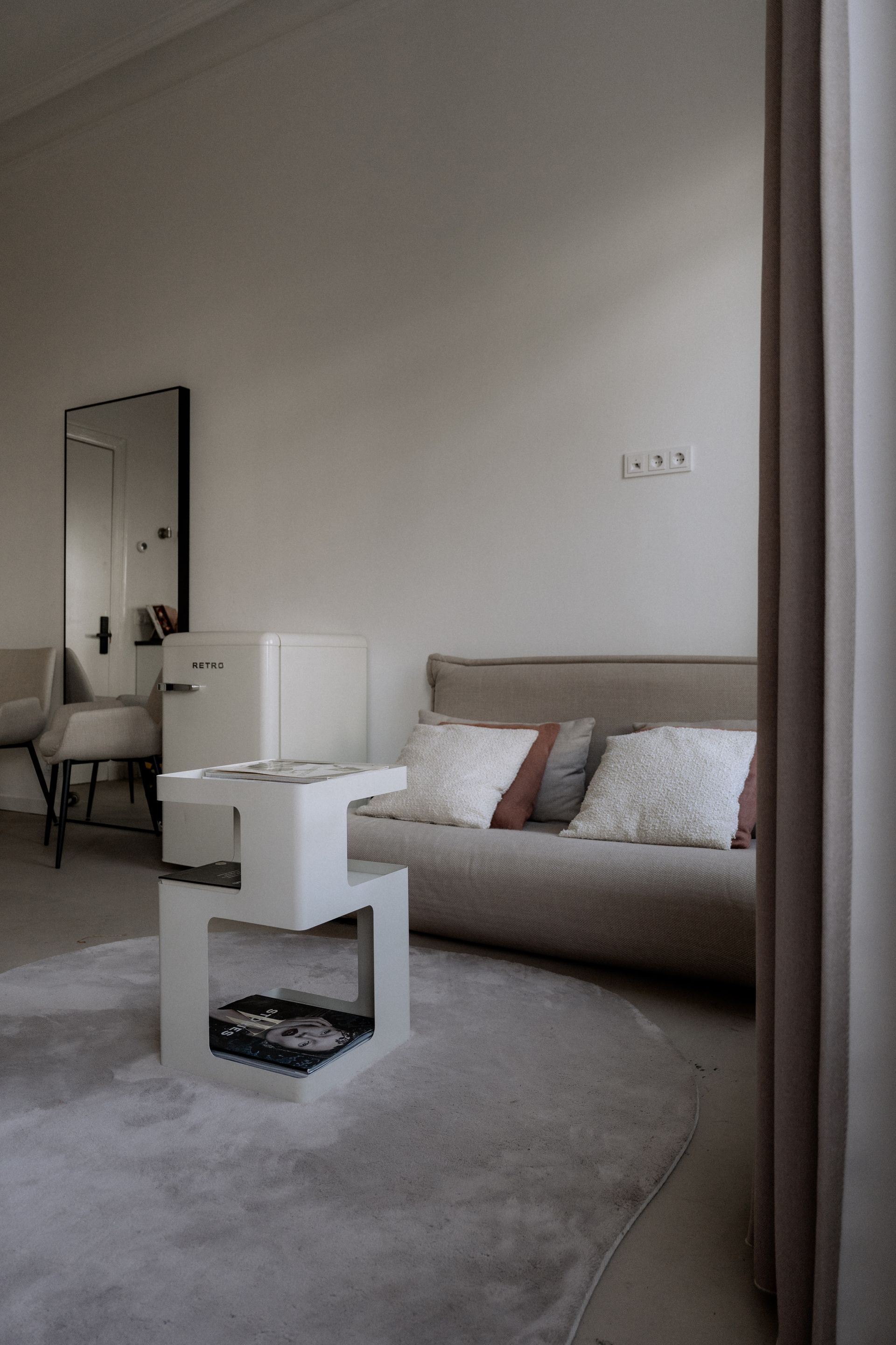 Minimalistische woonkamer met een bank, een moderne witte tafel, een spiegel en een grijs vloerkleed.
