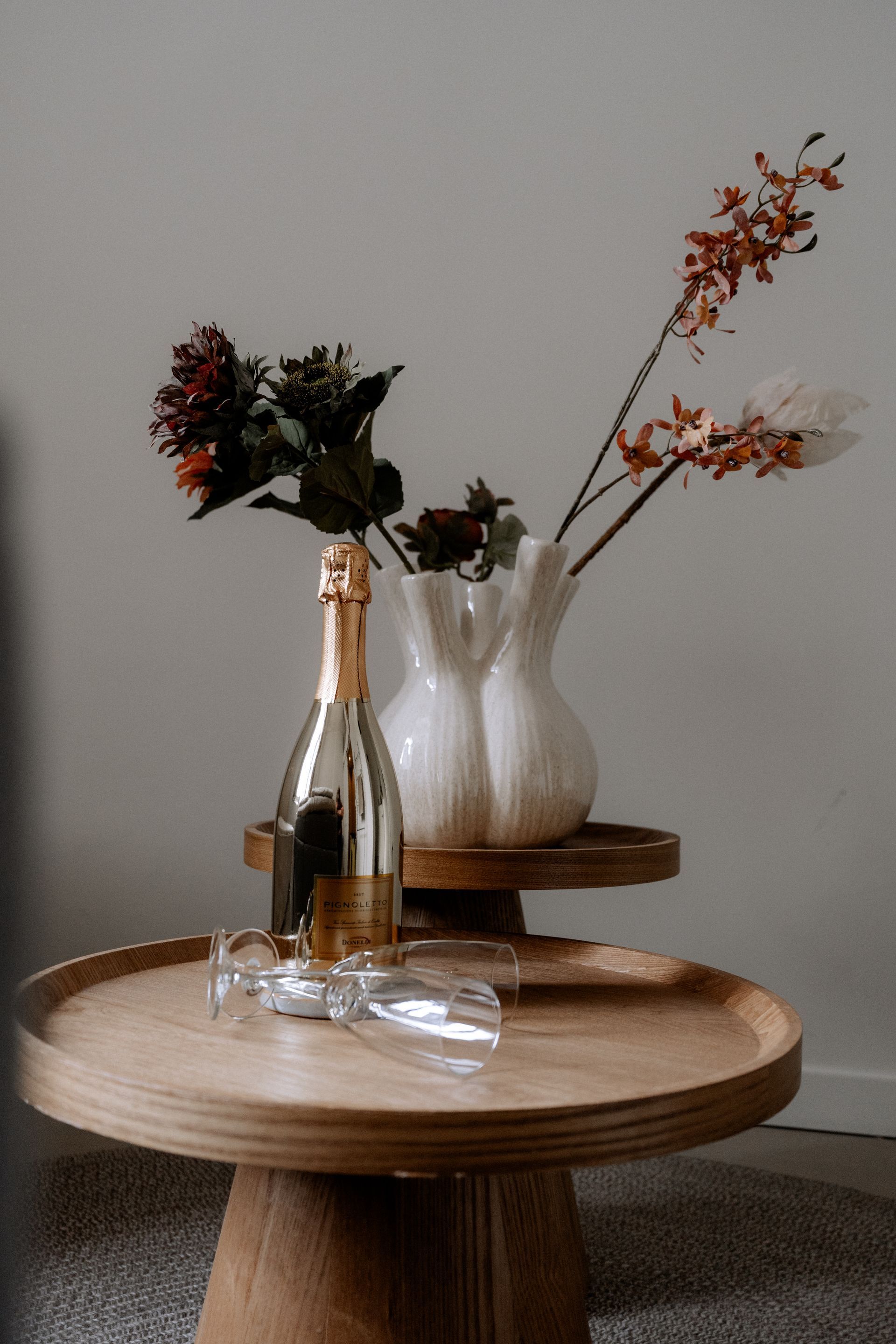 Een fles champagne en twee glazen op een houten tafel, met bloemen in een witte vaas.