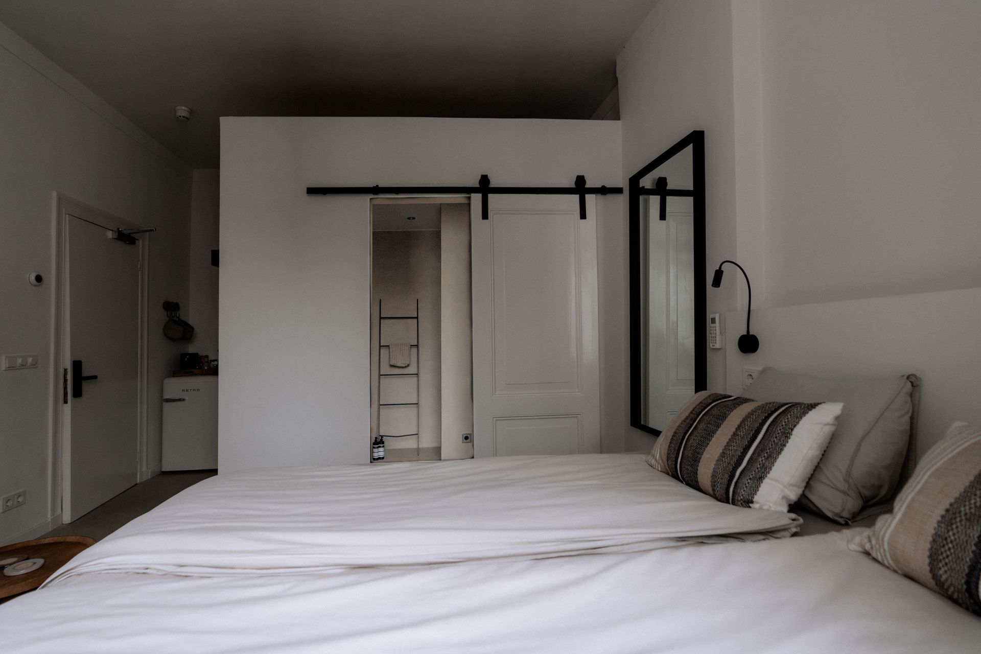 Slaapkamer met wit beddengoed, schuifdeur naar de badkamer en een spiegel met zwarte lijst.