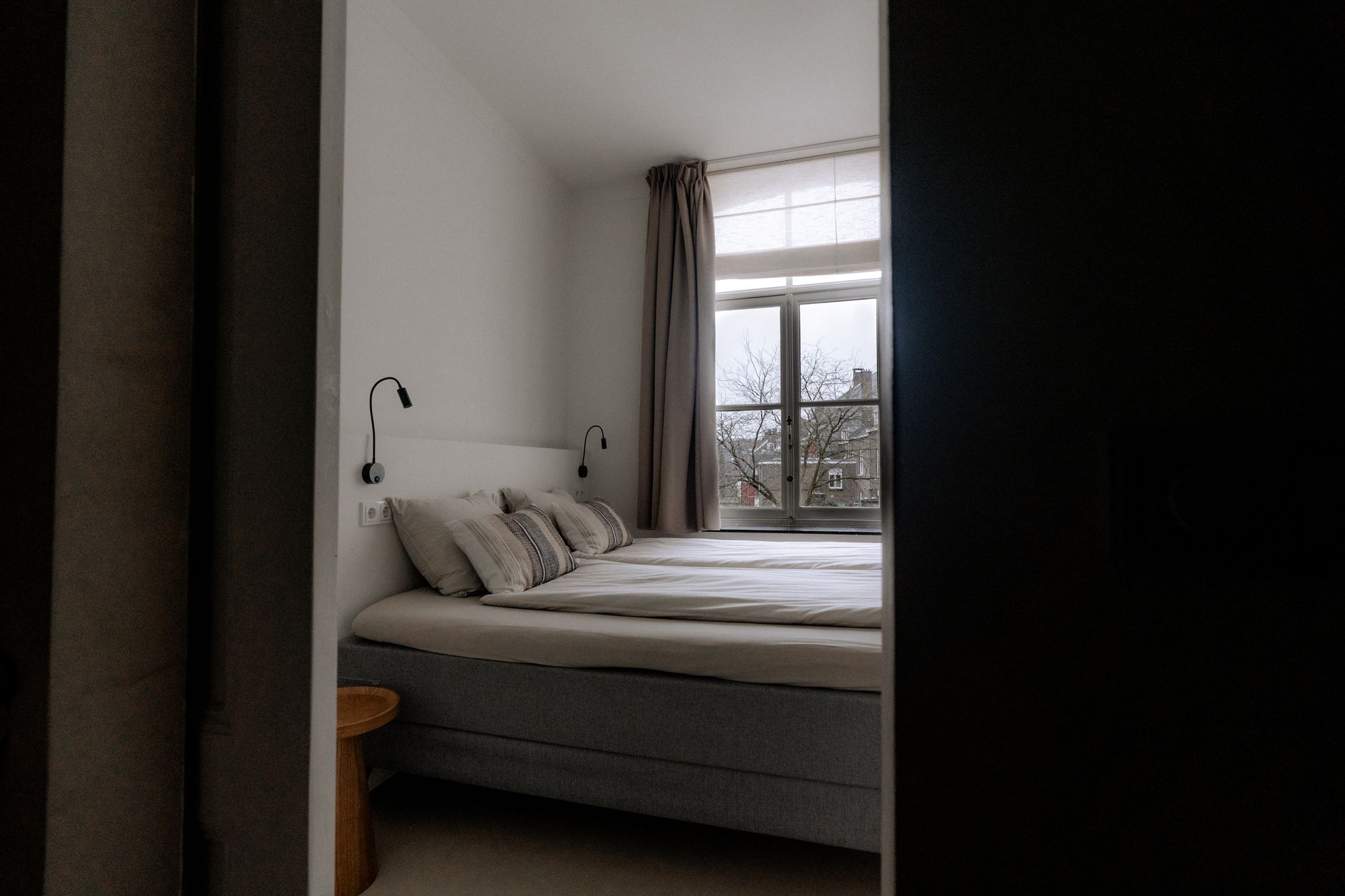 Slaapkamer met een bed, kussens en een raam met gordijnen; zichtbaar vanuit een deuropening.