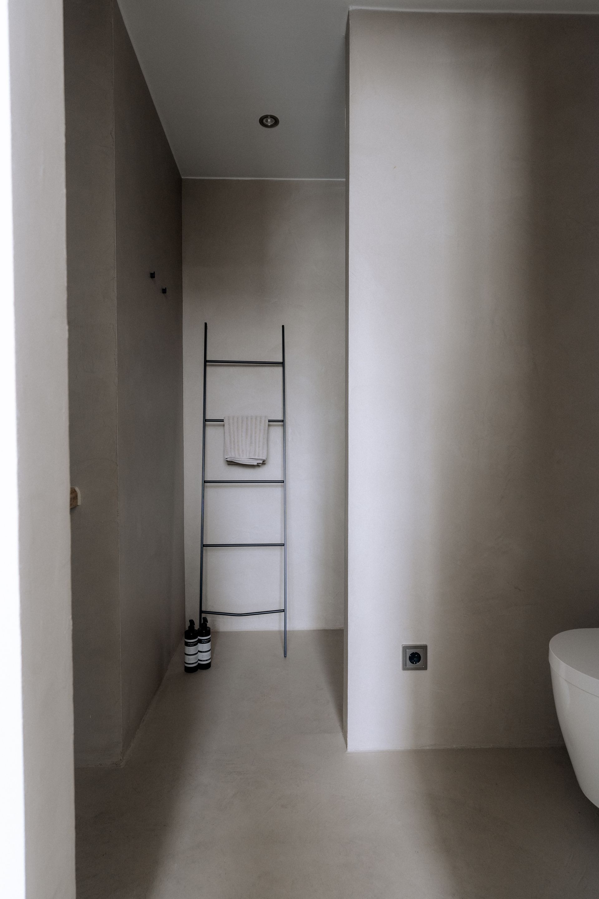 Beige minimalistische badkamer met een ladder voor handdoeken en een toilet.