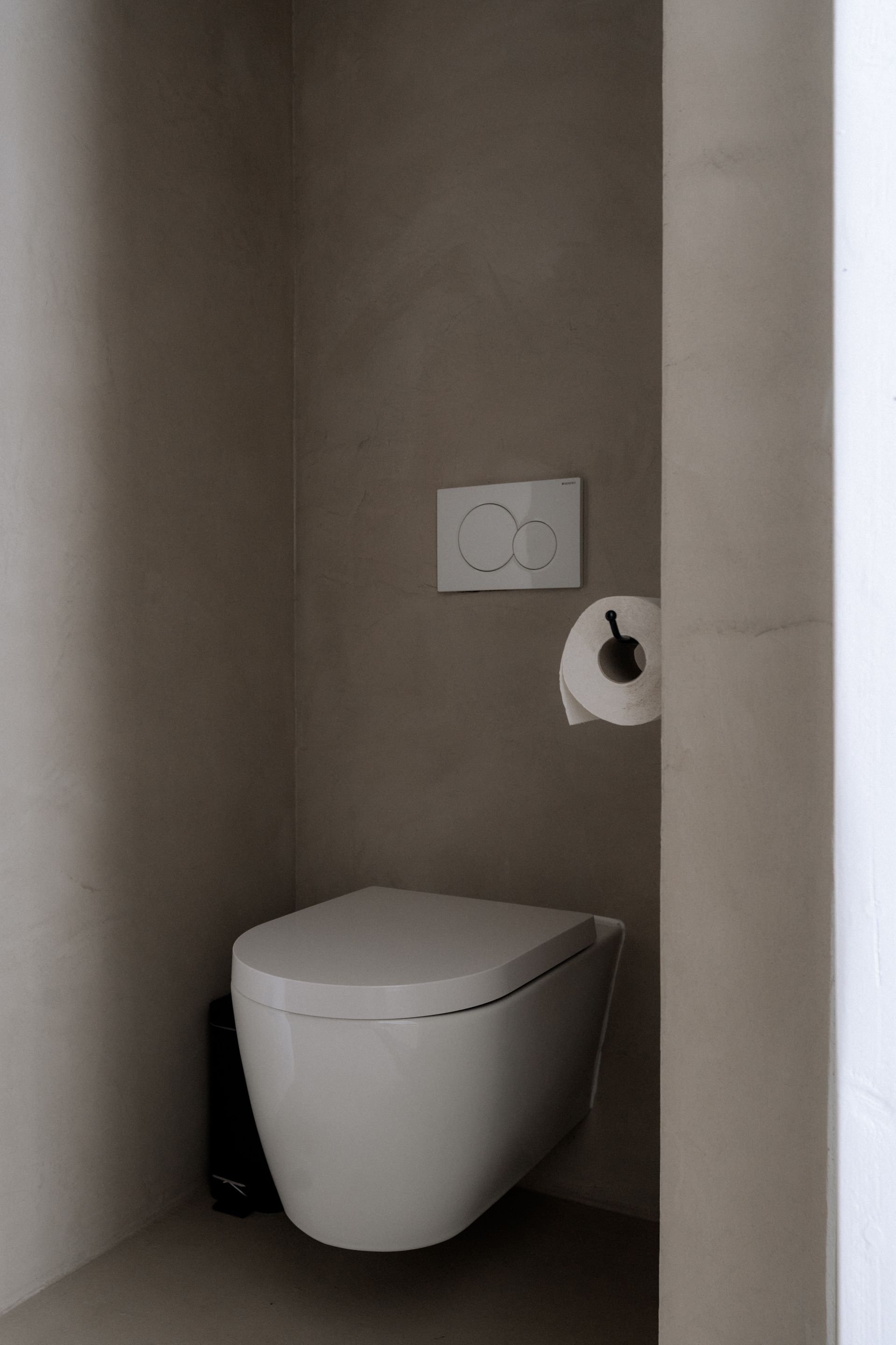Moderne, minimalistische badkamer met een wandtoilet, grijze muren en toiletpapier.
