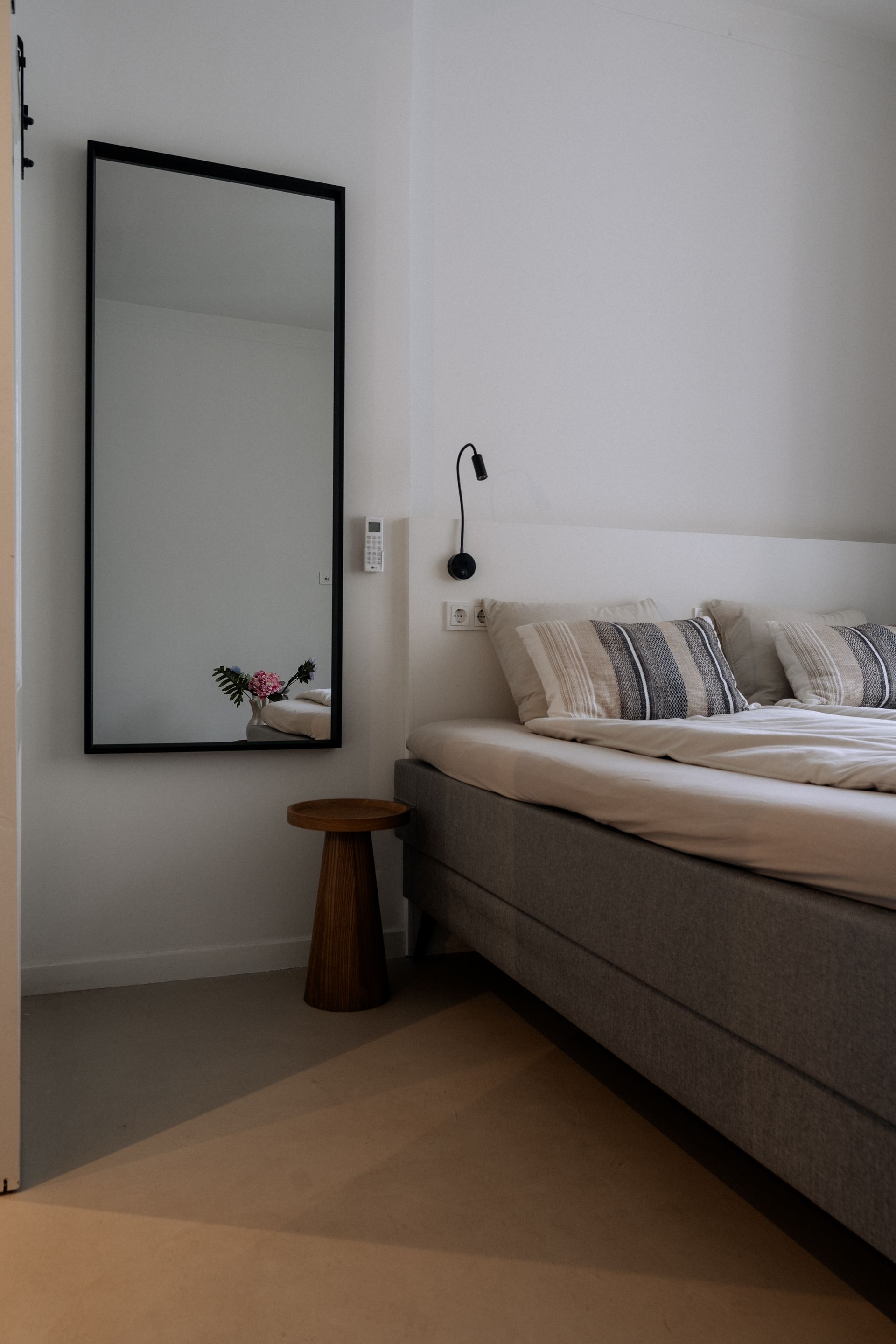 Slaapkamerinterieur met een grote spiegel, bed en een klein houten krukje.