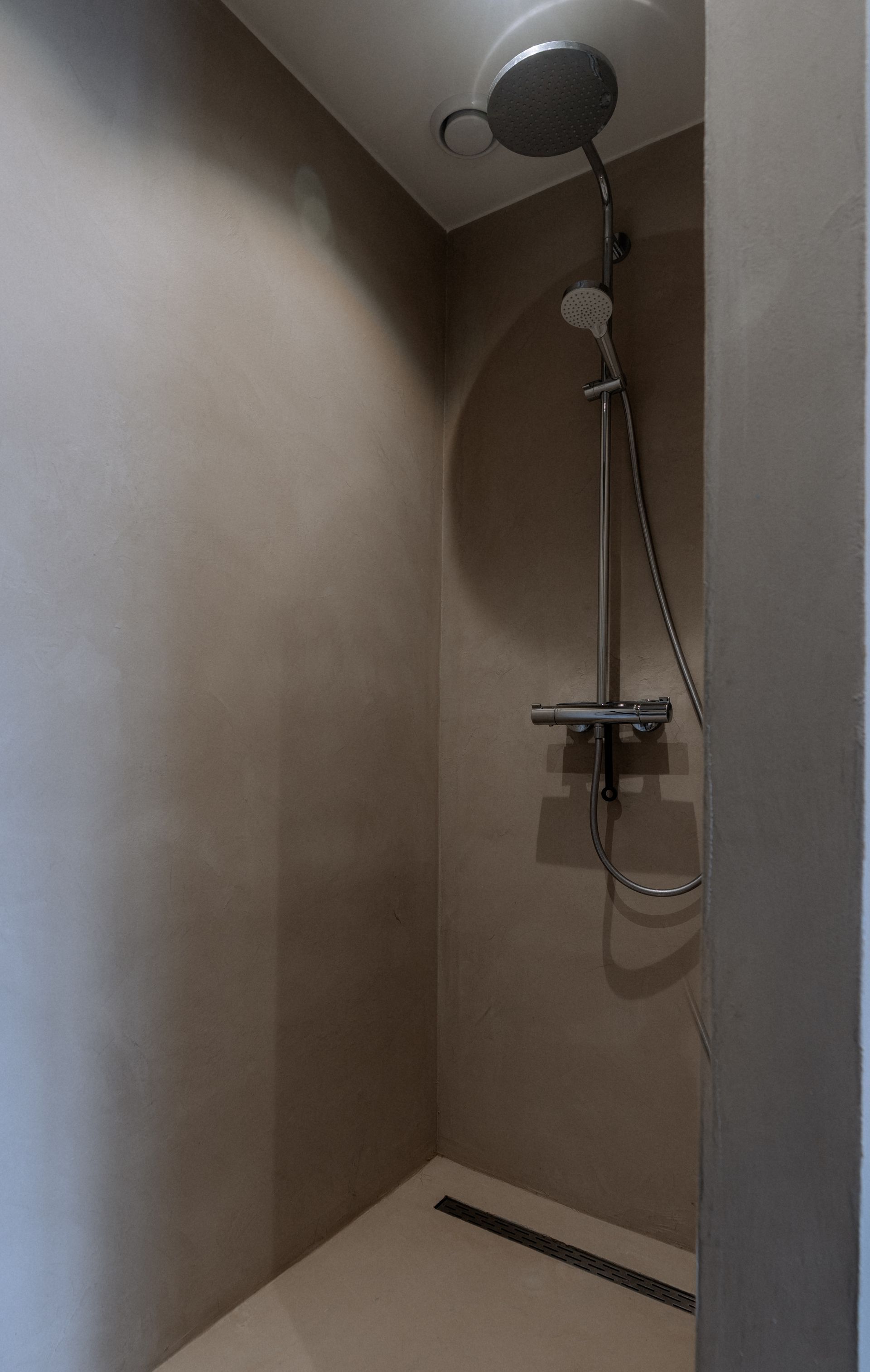 Kleine douche met een afgeronde bovenkant, lichtbruine wanden, chromen douchekop en kranen, en een afvoer.