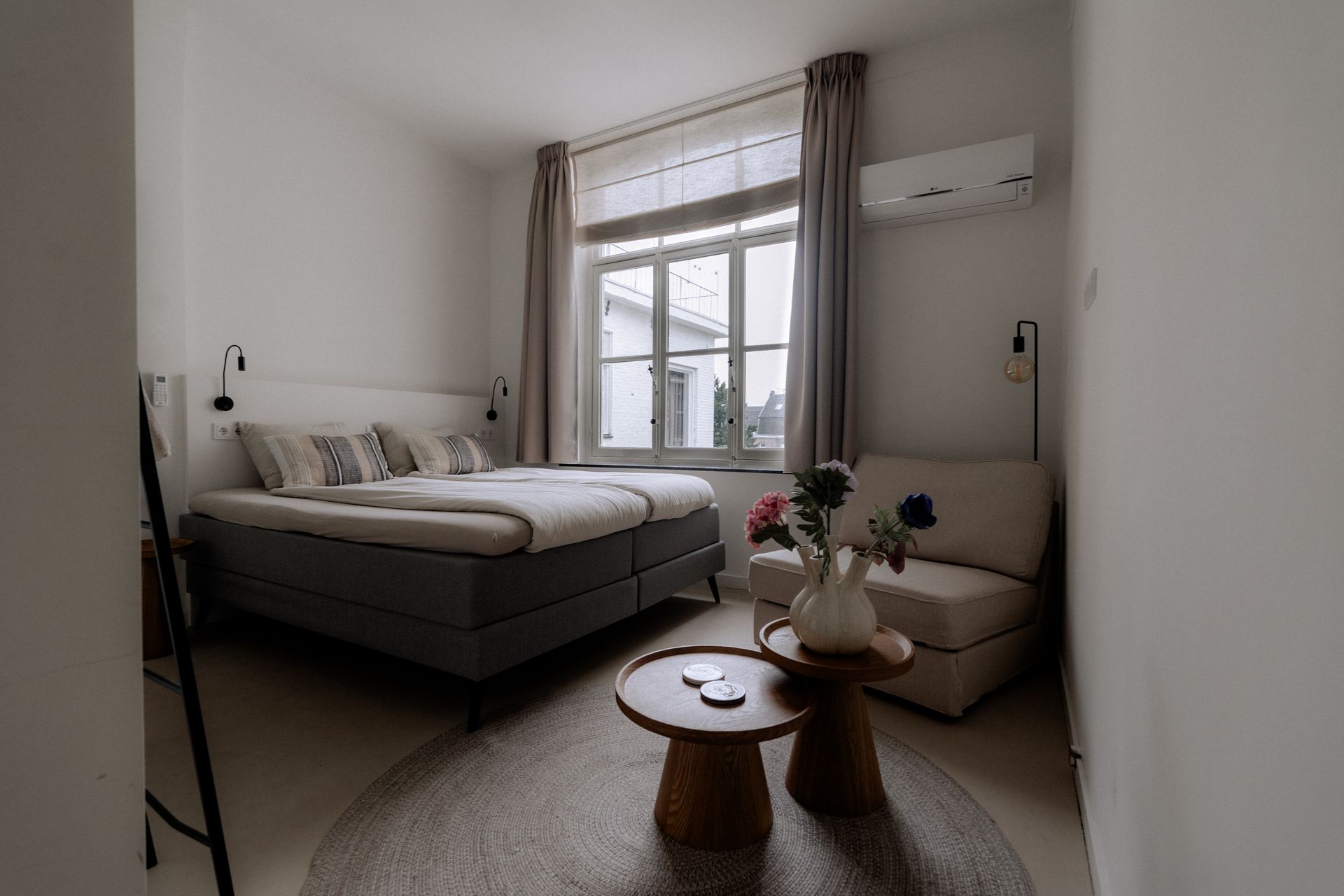 Slaapkamer met bed, kleine bank, ronde tafel en een raam.