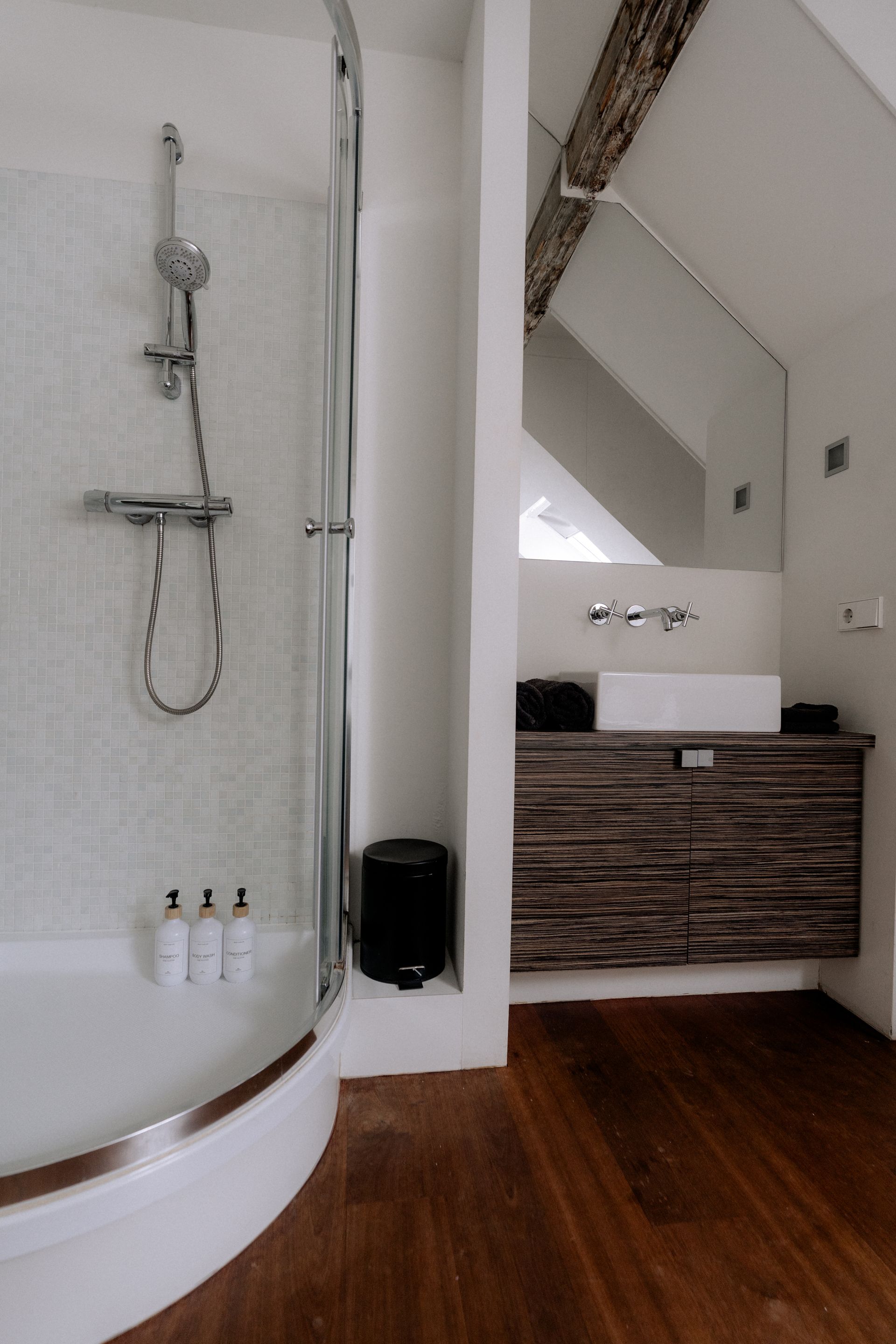 Moderne badkamer met gebogen douche, houten wastafelmeubel en witte muren.