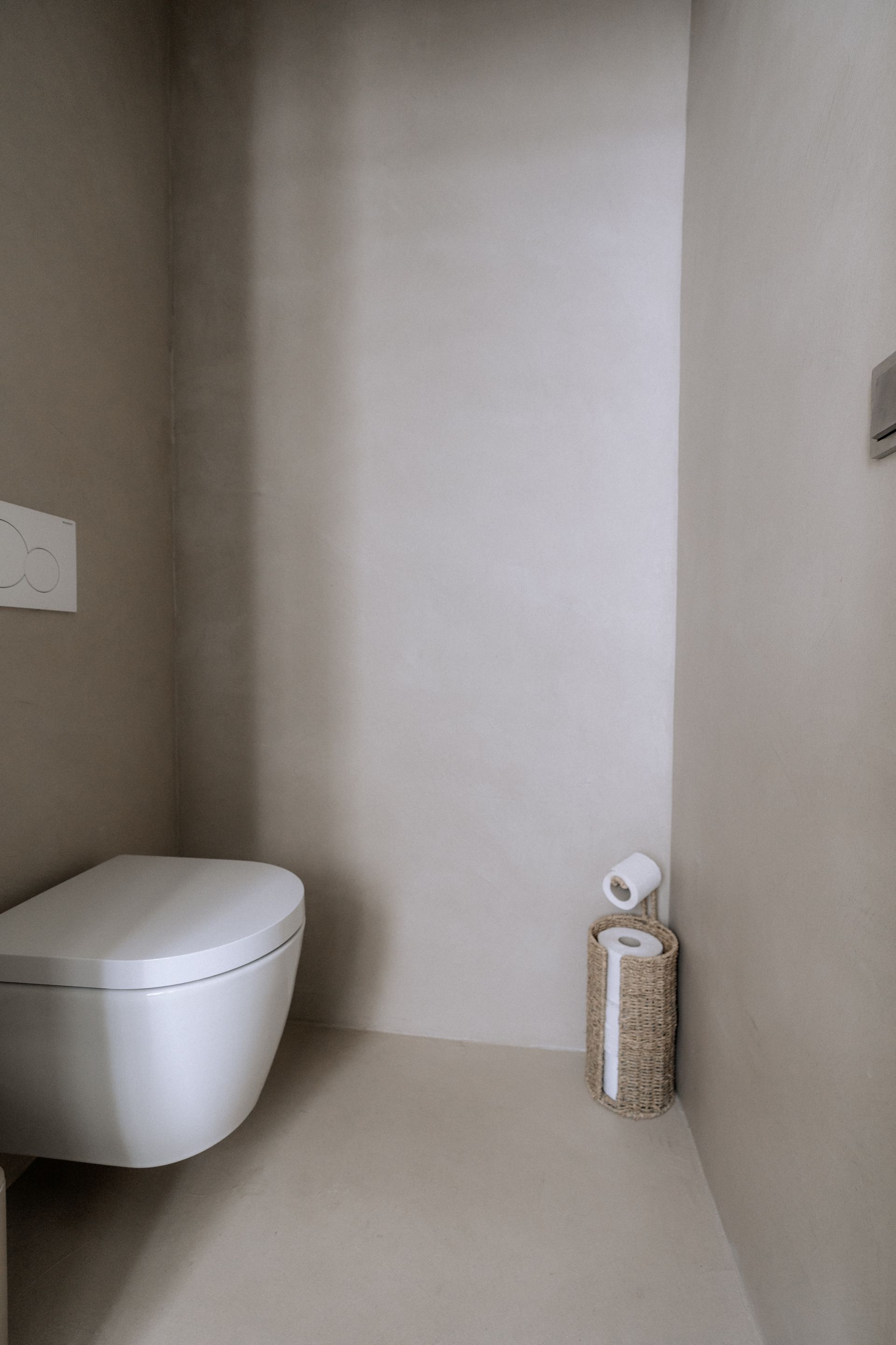 Moderne, minimalistische badkamer met een wit toilet en een decoratieve toiletpapierhouder. Beige muren en vloer.