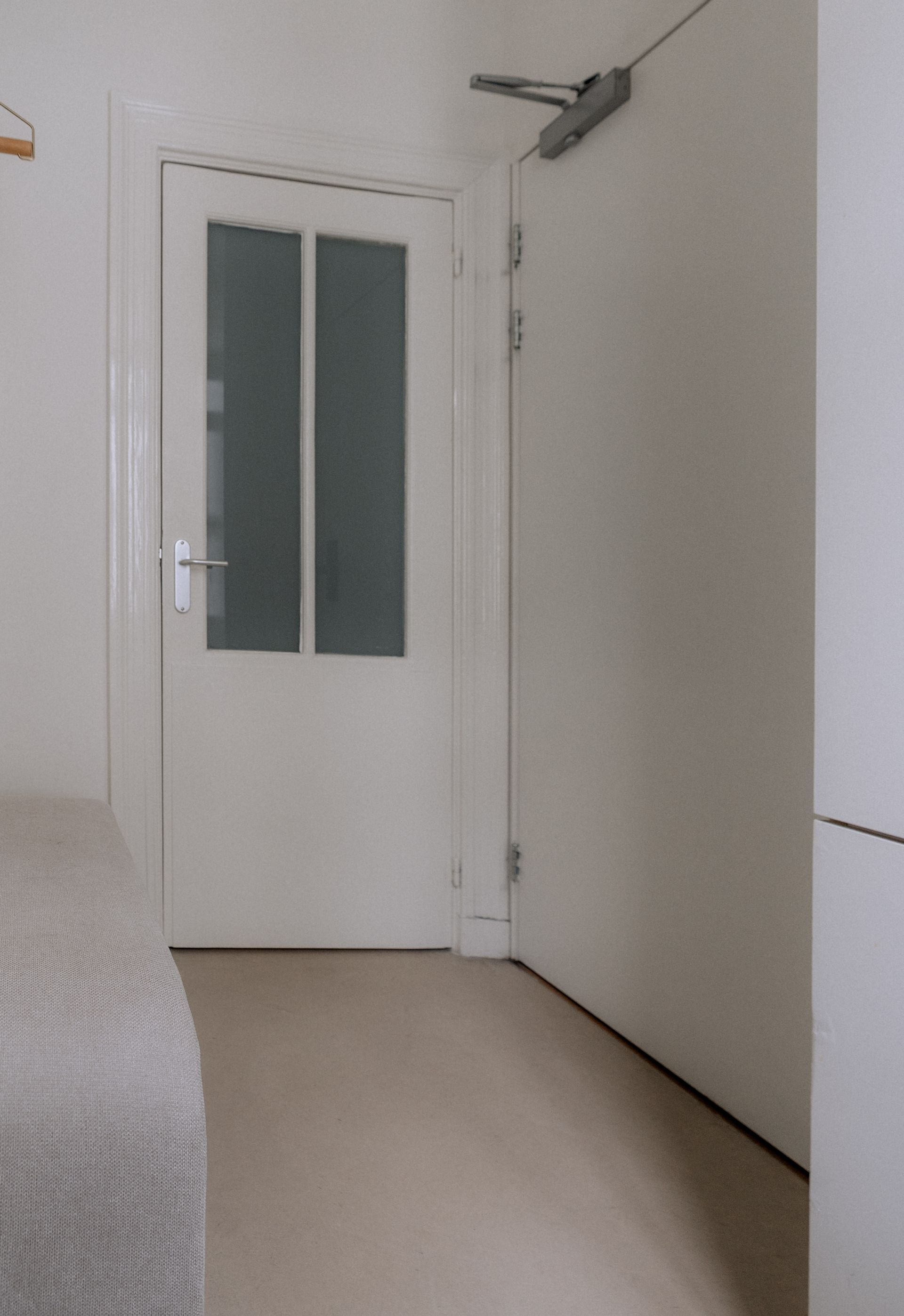 Witte deur met matglazen panelen, naast een effen witte deur in een lichtgekleurde kamer.