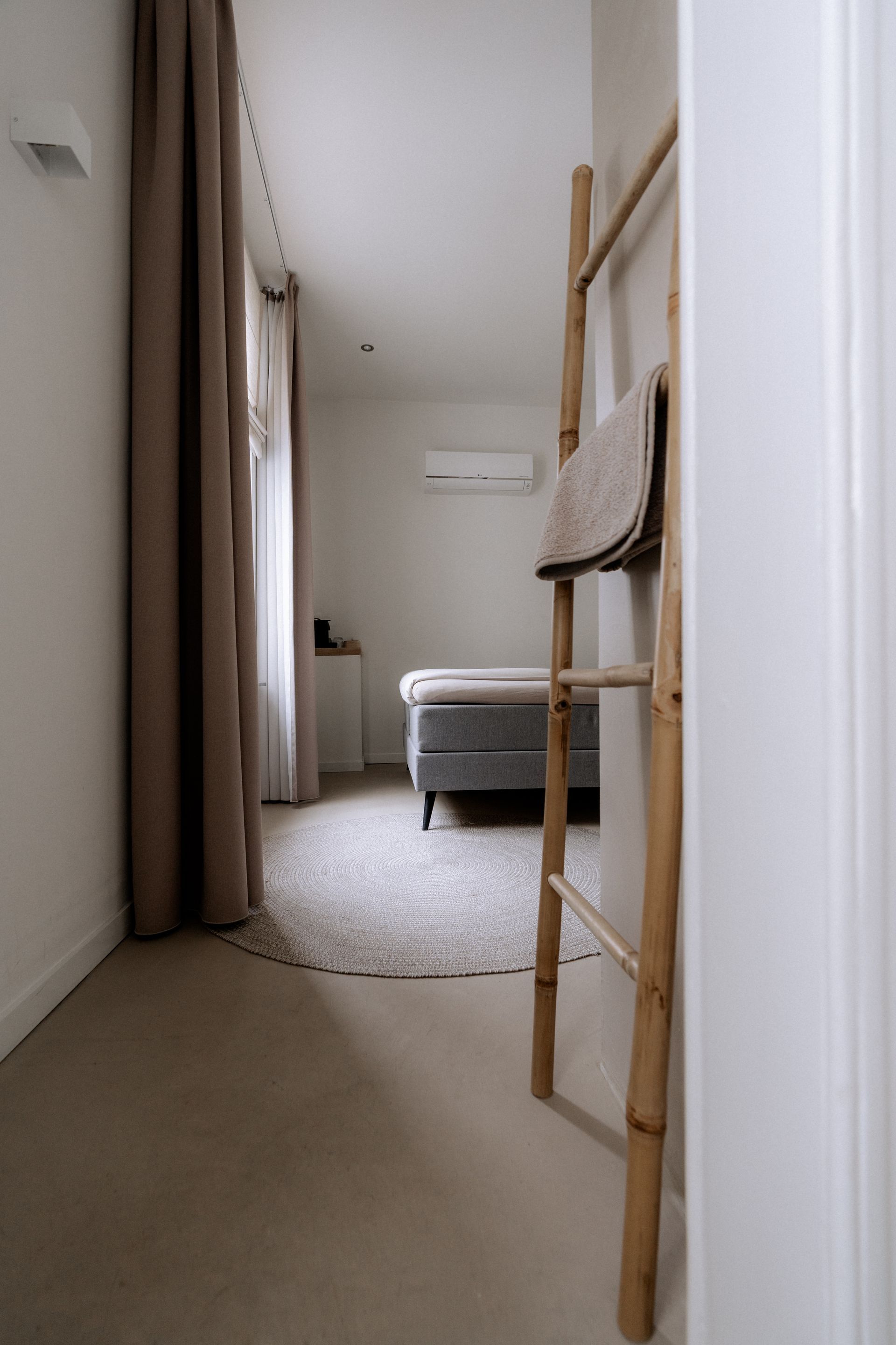 Smalle slaapkamer met bed, vloerkleed en een houten ladder tegen de muur.