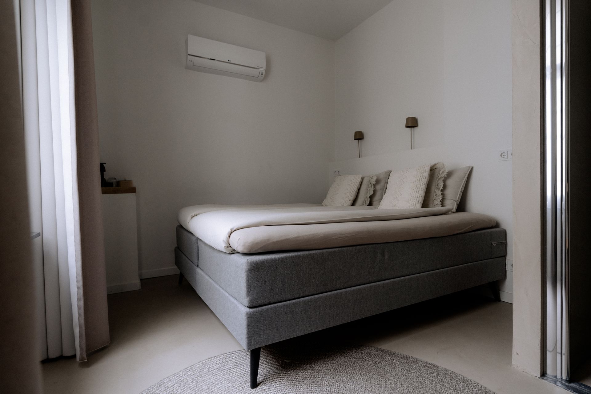 Slaapkamer met een grijs bed, witte muren en airconditioning.