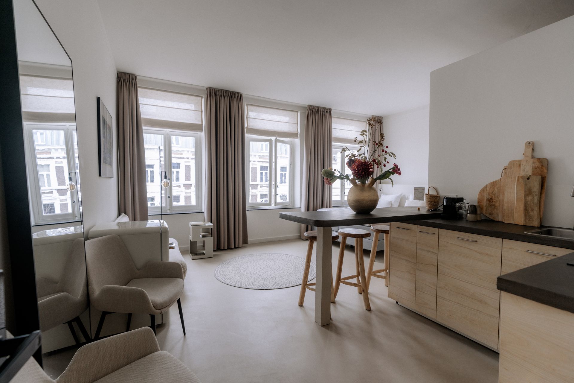 Gezellig appartementinterieur met een eettafel, stoelen, ramen met gordijnen en een keukenblad.