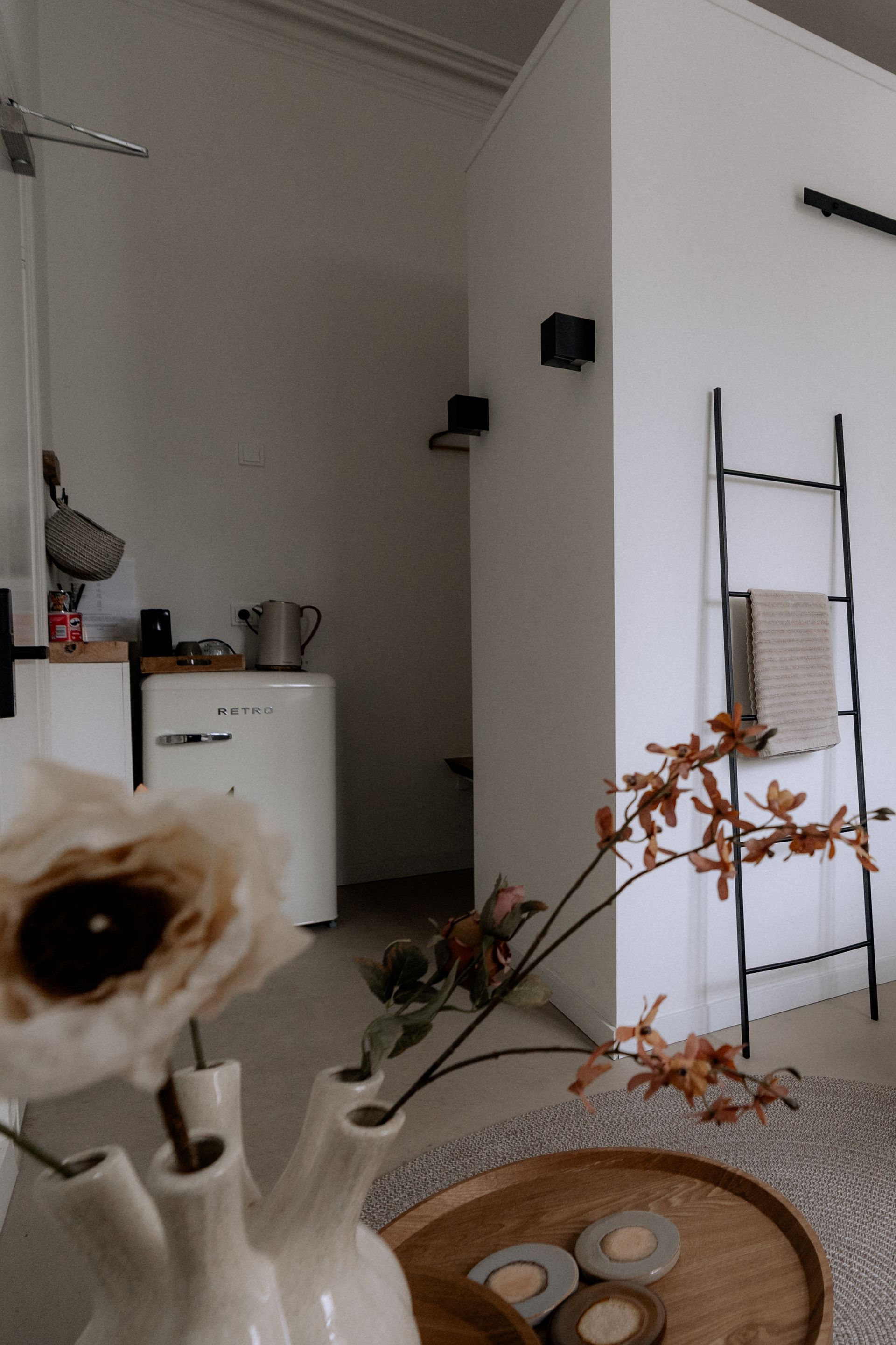 Witte kamer met decoratieve bloemenvaas, kleine koelkast en een scheve ladder.