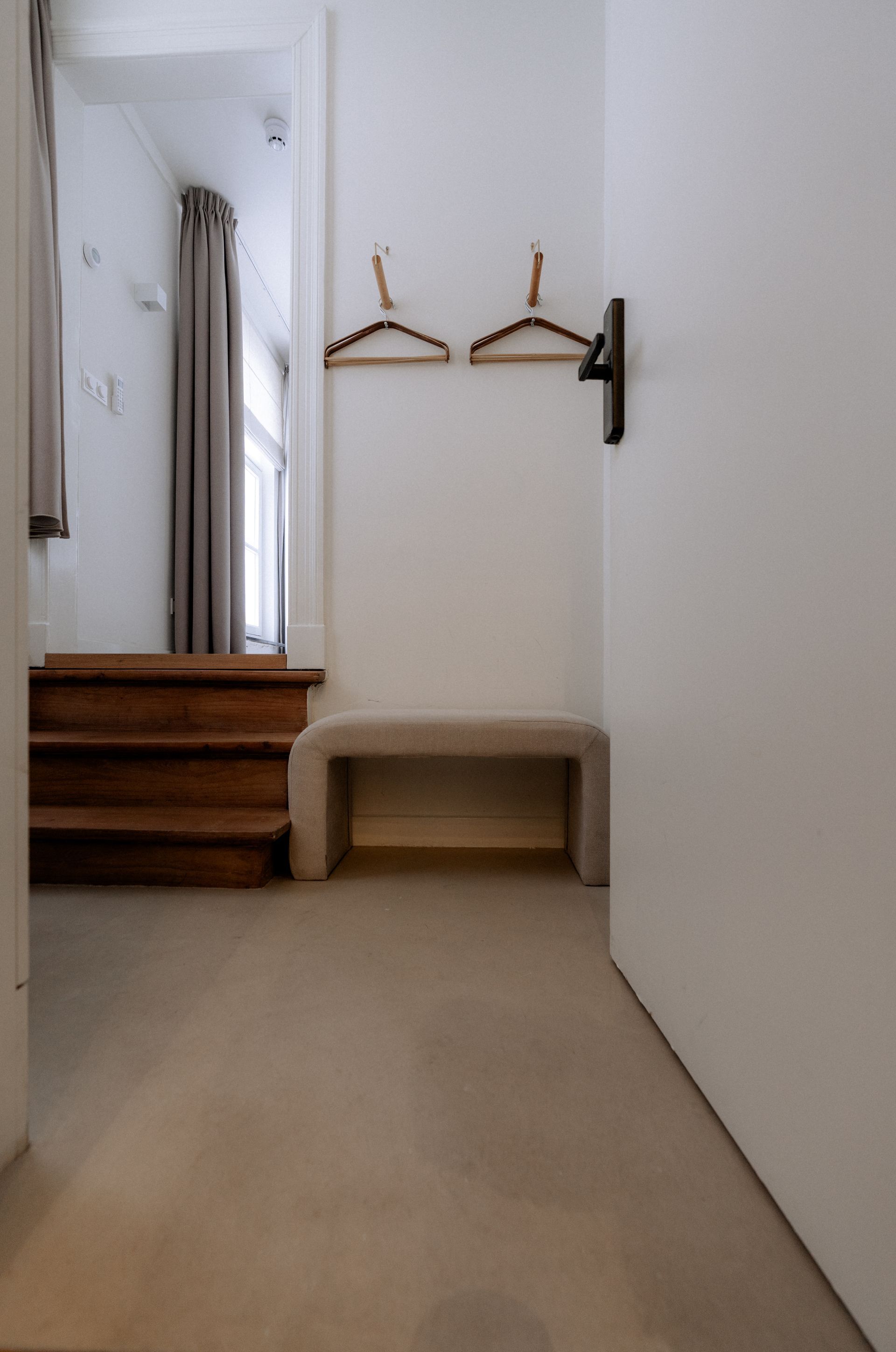 Entree met bankje, twee houten kapstokken en een trap naar kamer. Houten treden en een mooie vloer.