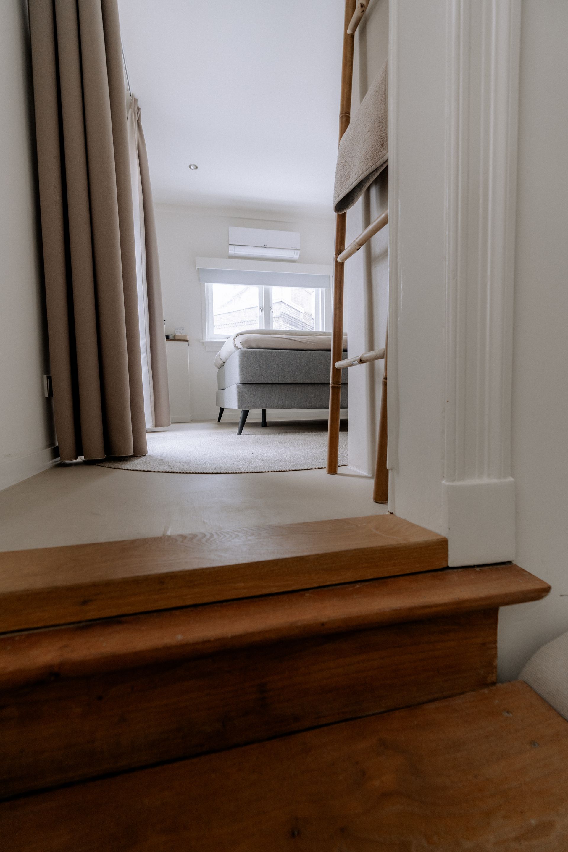 Een houten trap leidt naar een lichte kamer met een bed, een raam en een decoratieve ladder.