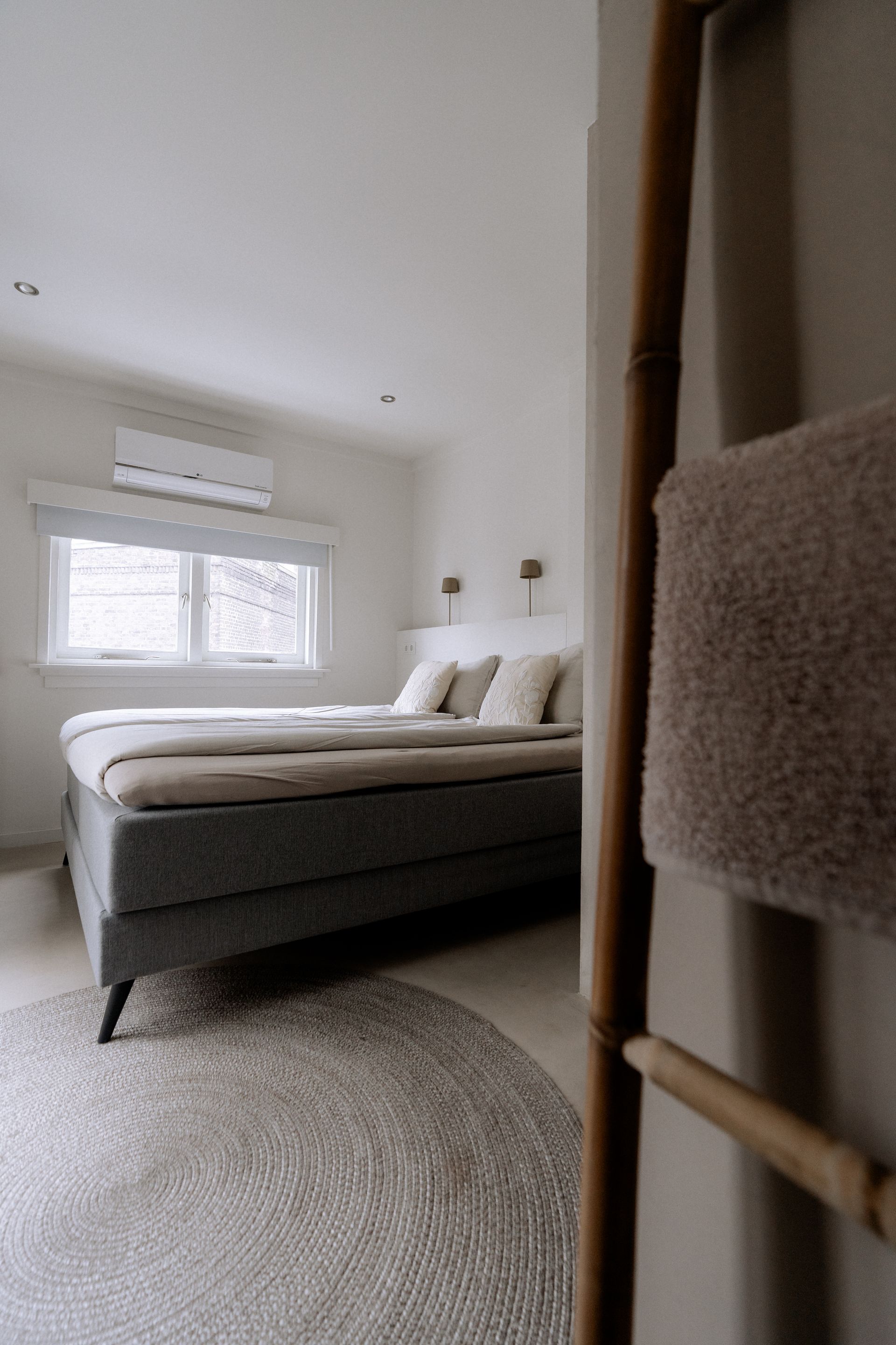 Slaapkamer met een grijs bed, een rond vloerkleed en een houten ladder met een handdoek.