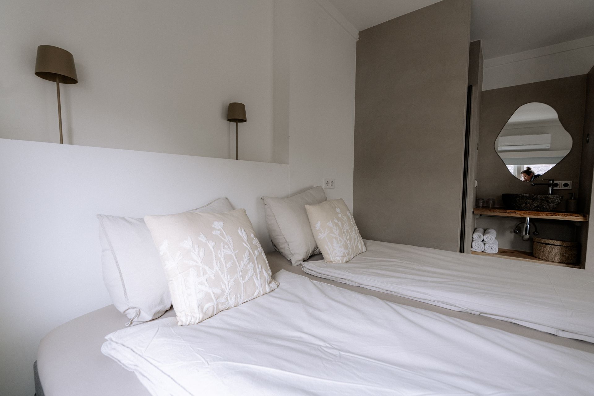 Twee eenpersoonsbedden in een minimalistische kamer met wit beddengoed en een badkamer zichtbaar op de achtergrond.