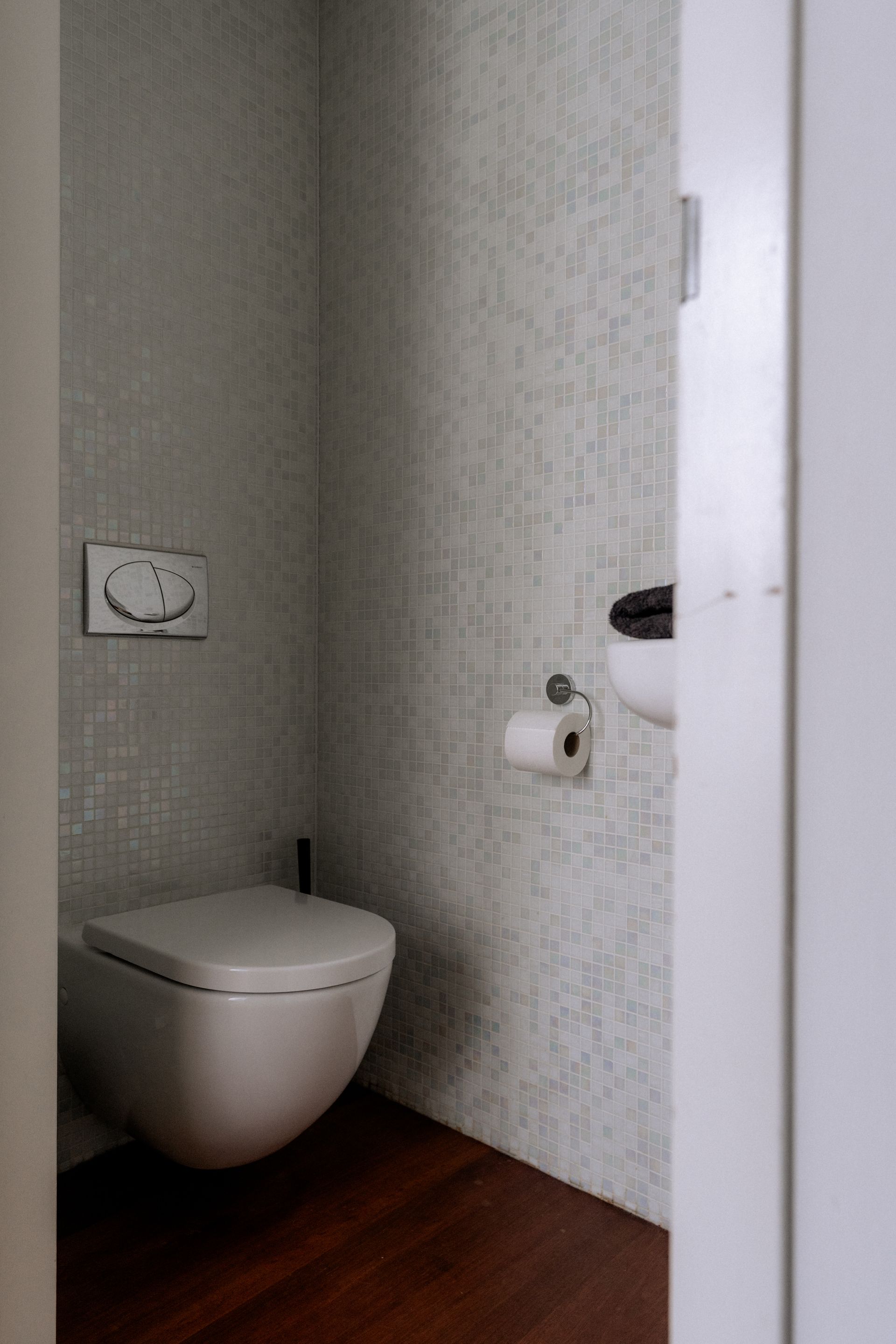 Een kleine, moderne badkamer met een wit, aan de muur gemonteerd toilet. Licht behang en een donkere houten vloer.