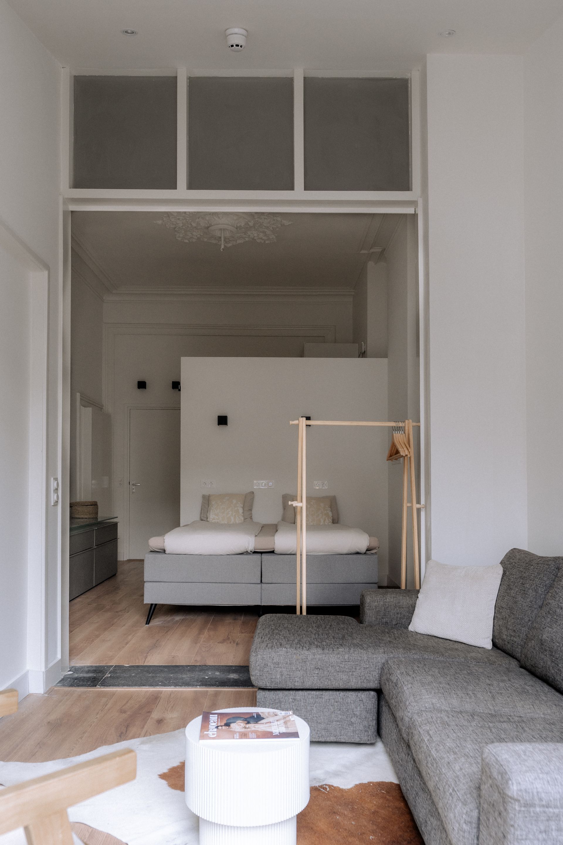 Modern appartementinterieur met open indeling, met een slaapkamer en woonkamer voorzien van een grijze bank en een bed.