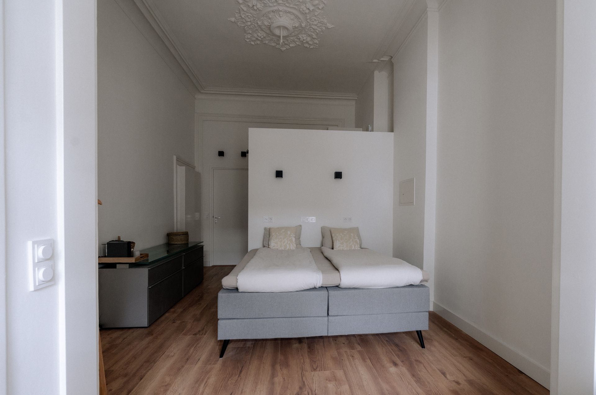 Slaapkamer met een bed, commode en een scheidingswand, alles in het wit met houten vloer.