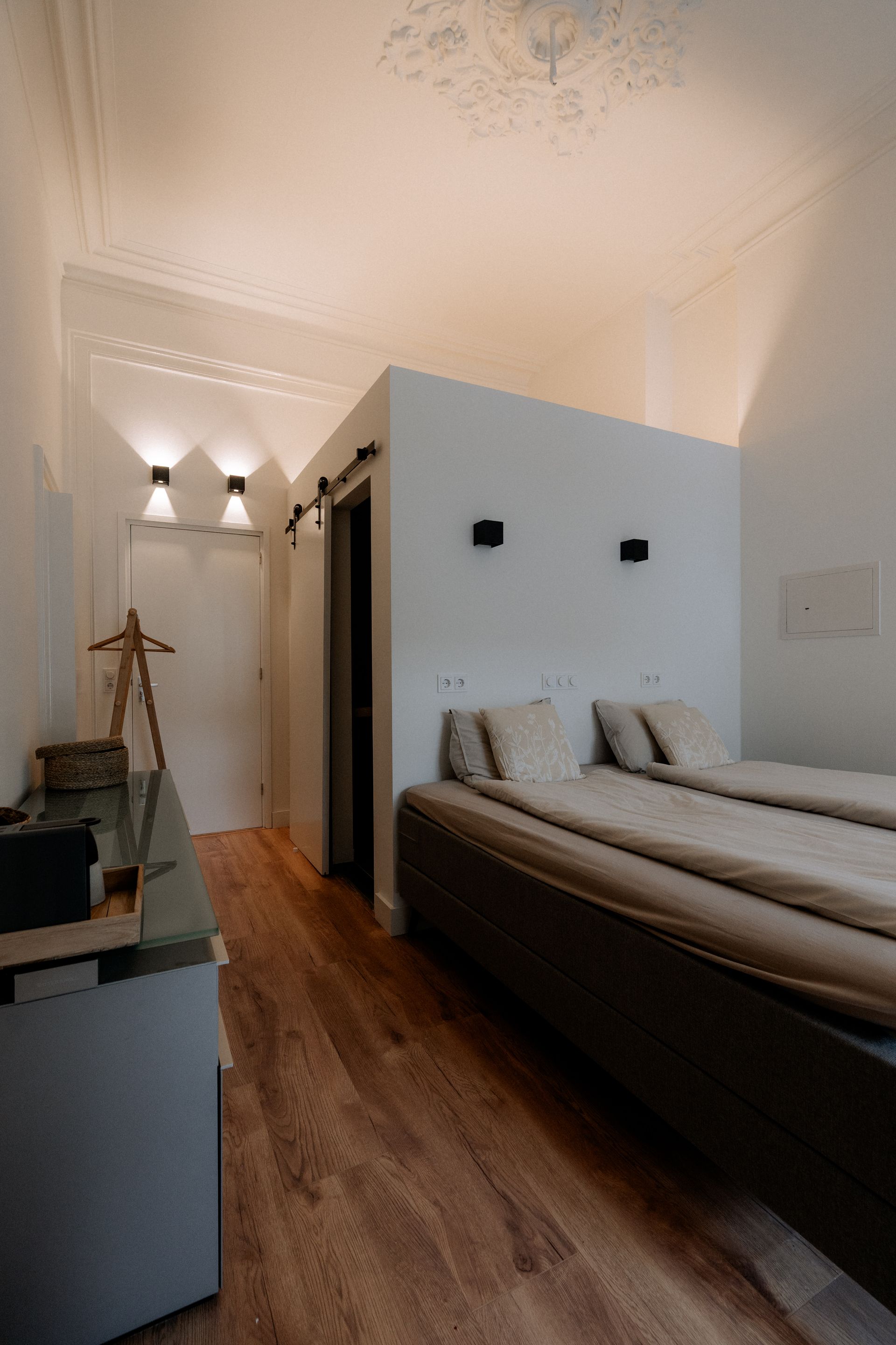 Slaapkamerinterieur met een bed, witte muren, houten vloer en plafondverlichting.