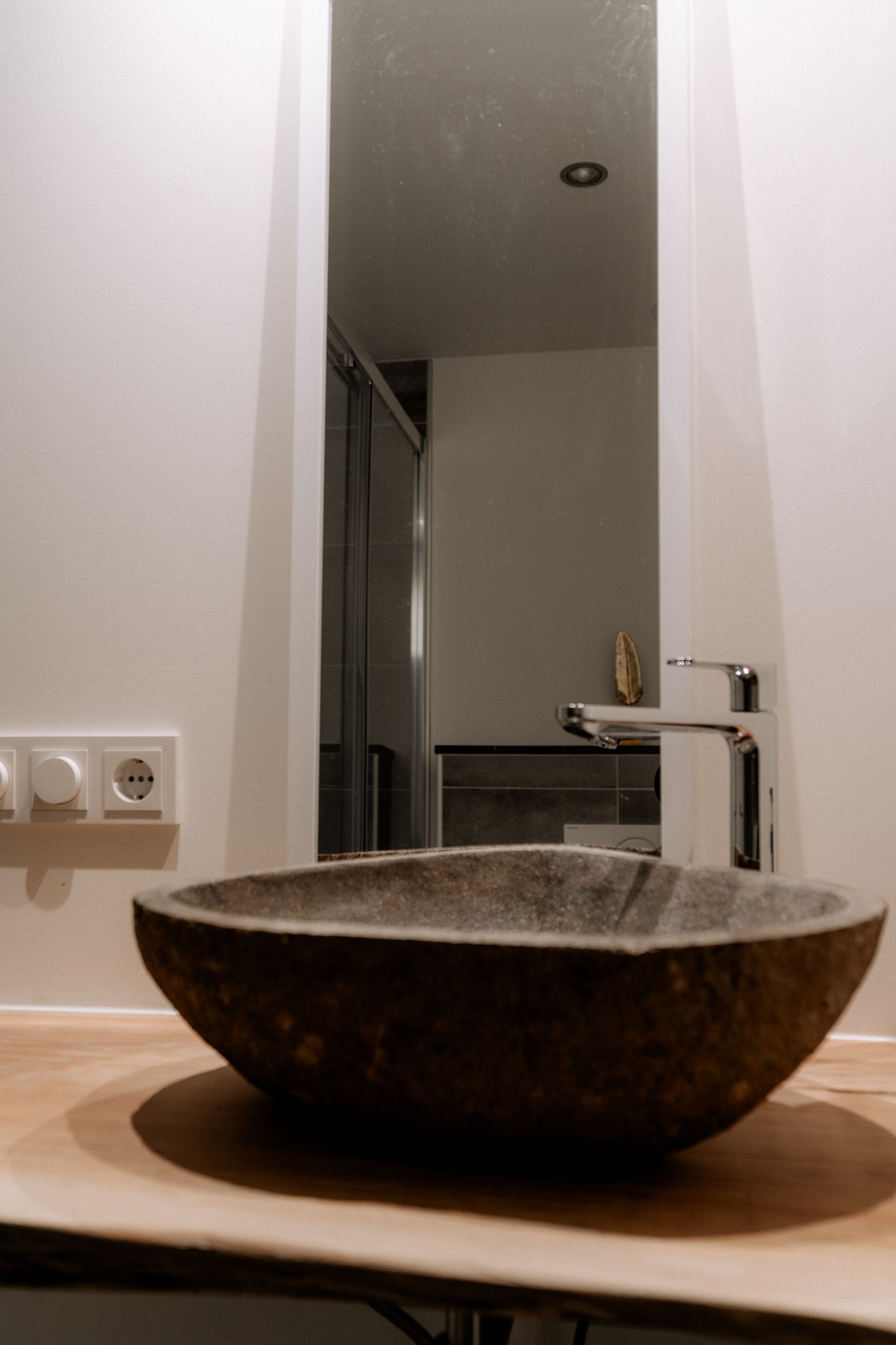 Badkamer met een donkere stenen wastafel, chromen kraan en rechthoekige spiegel.
