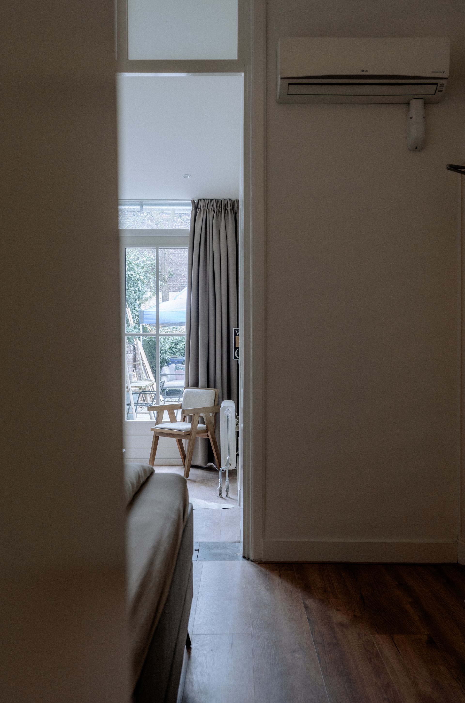 Gang die leidt naar een kamer met een raam, een stoel en gordijnen. Airconditioning aan de muur.
