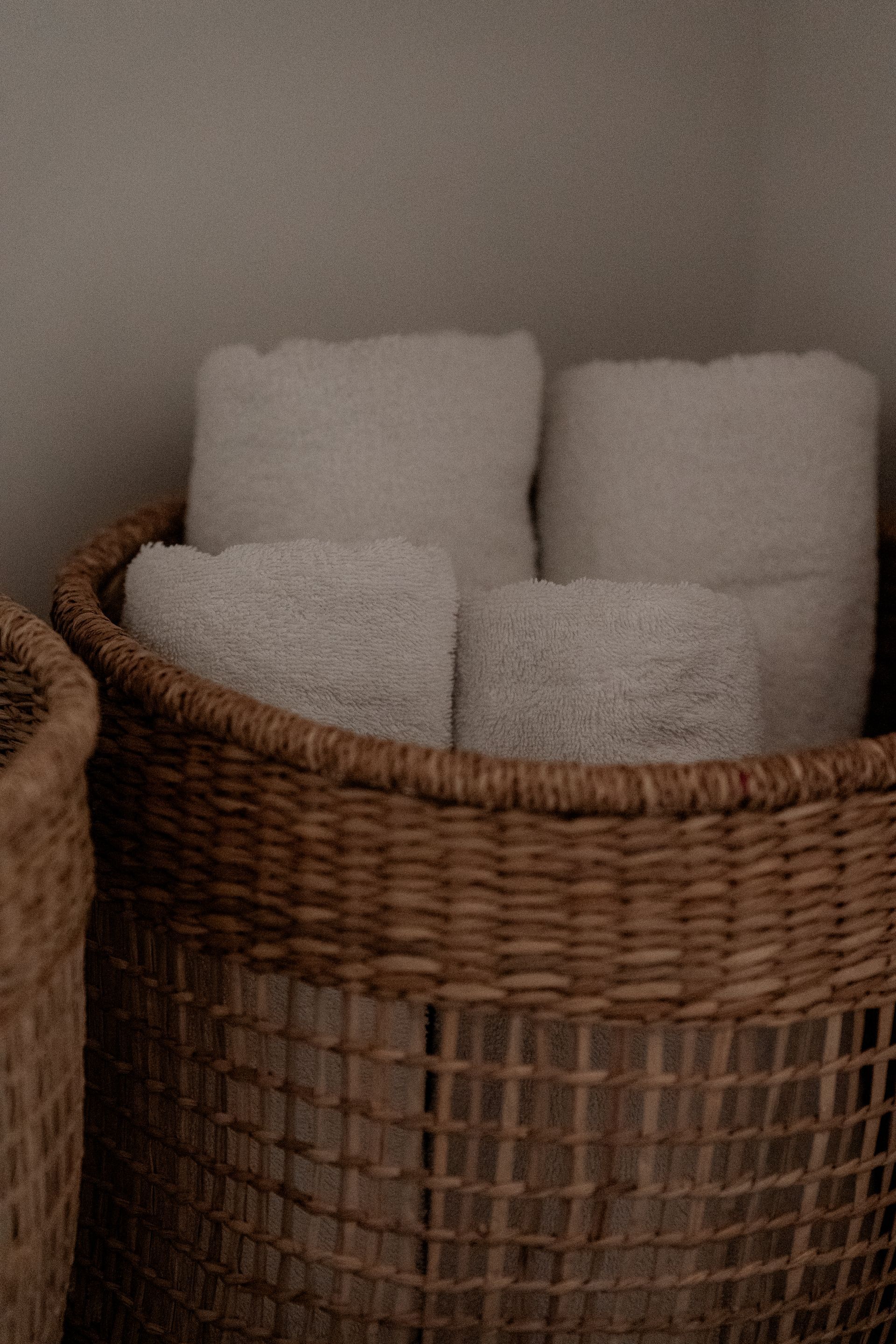 Een rieten mand gevuld met opgerolde witte handdoeken in een kamer met neutrale tinten.