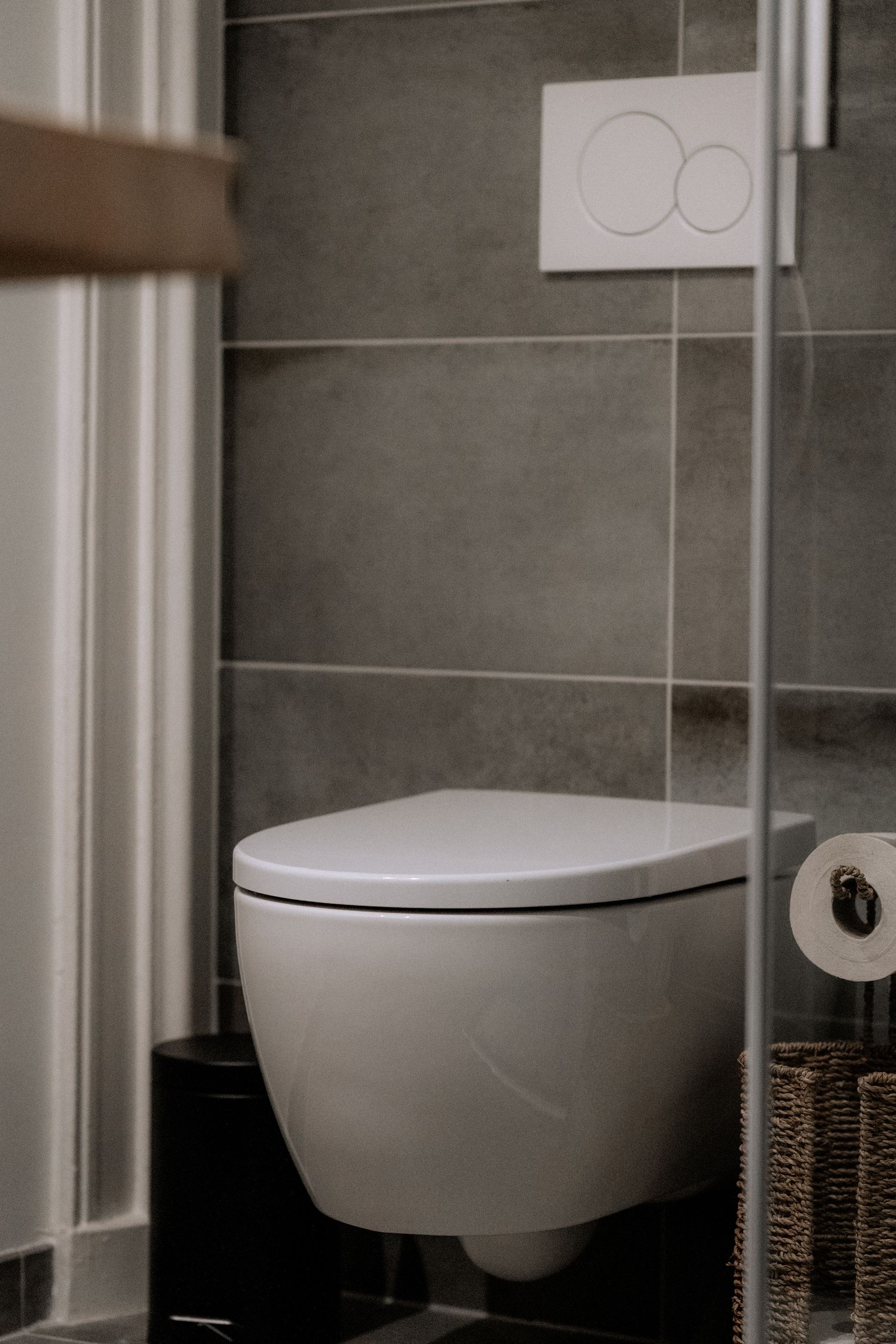 Wit wandtoilet in een moderne badkamer met grijze tegels en een witte bedieningsplaat.