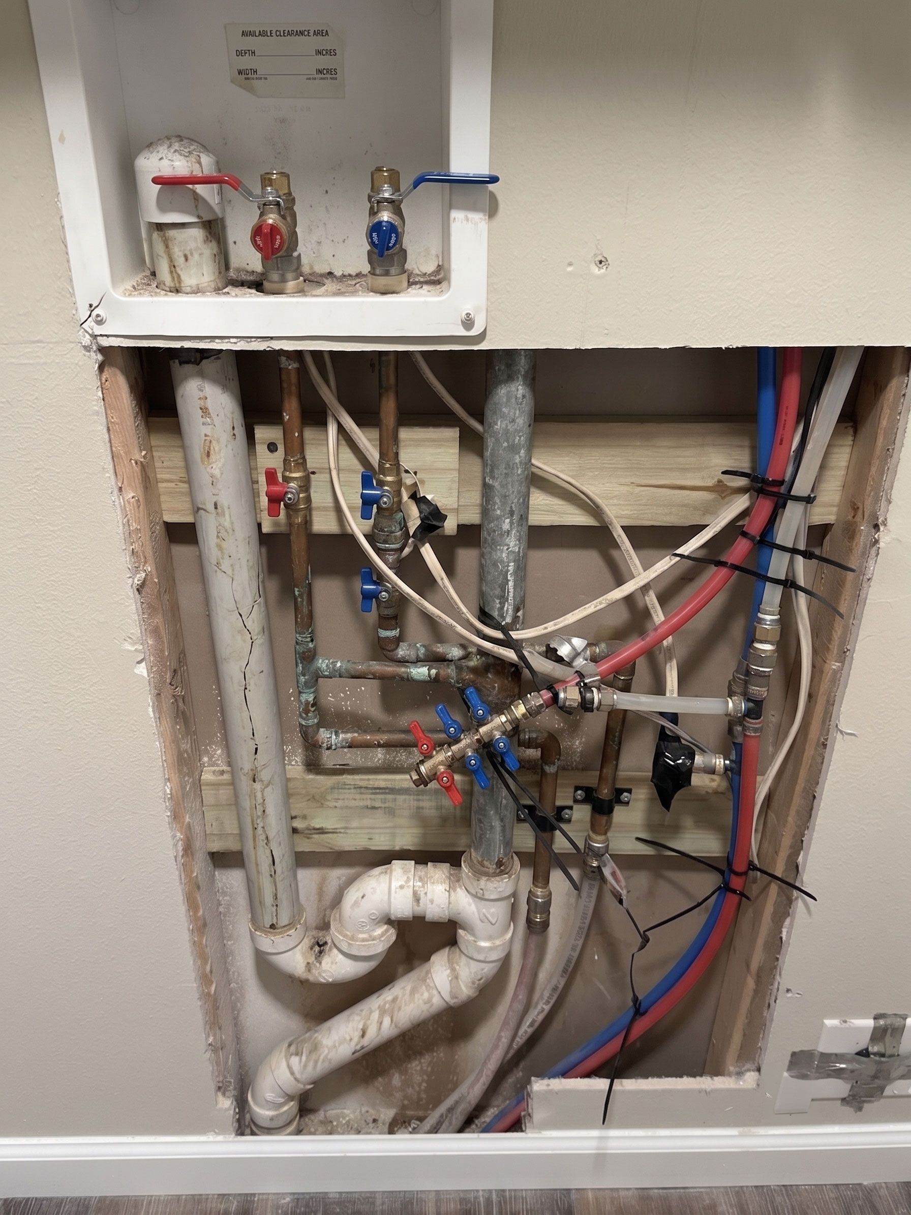 Open plumbing and valve assembly inside a wall cavity with red, blue, and white pipes.
