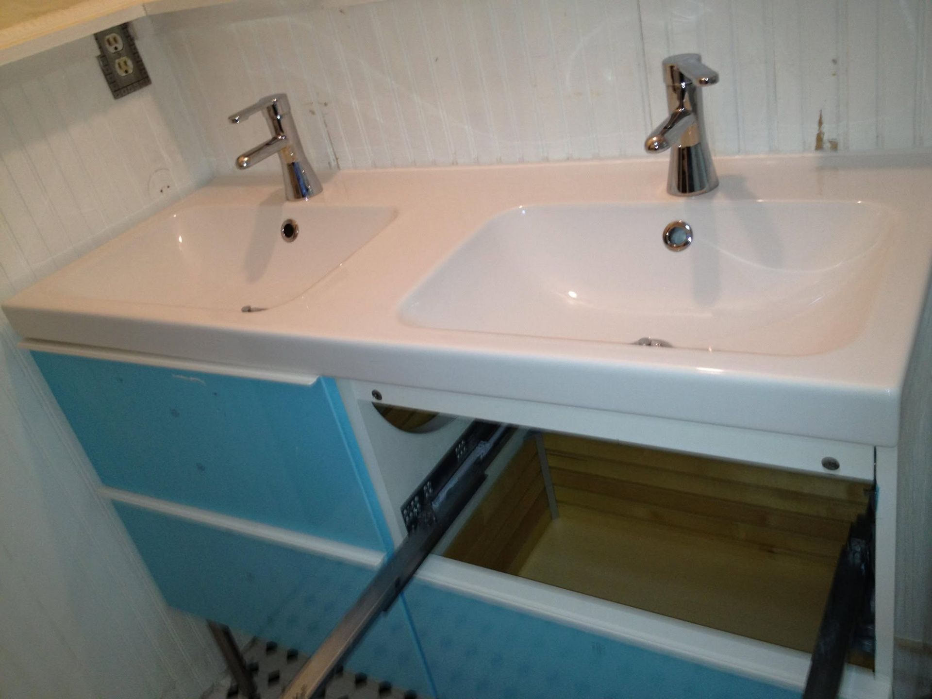 Bathroom vanity with double sinks, open drawers, and a blue cabinet
