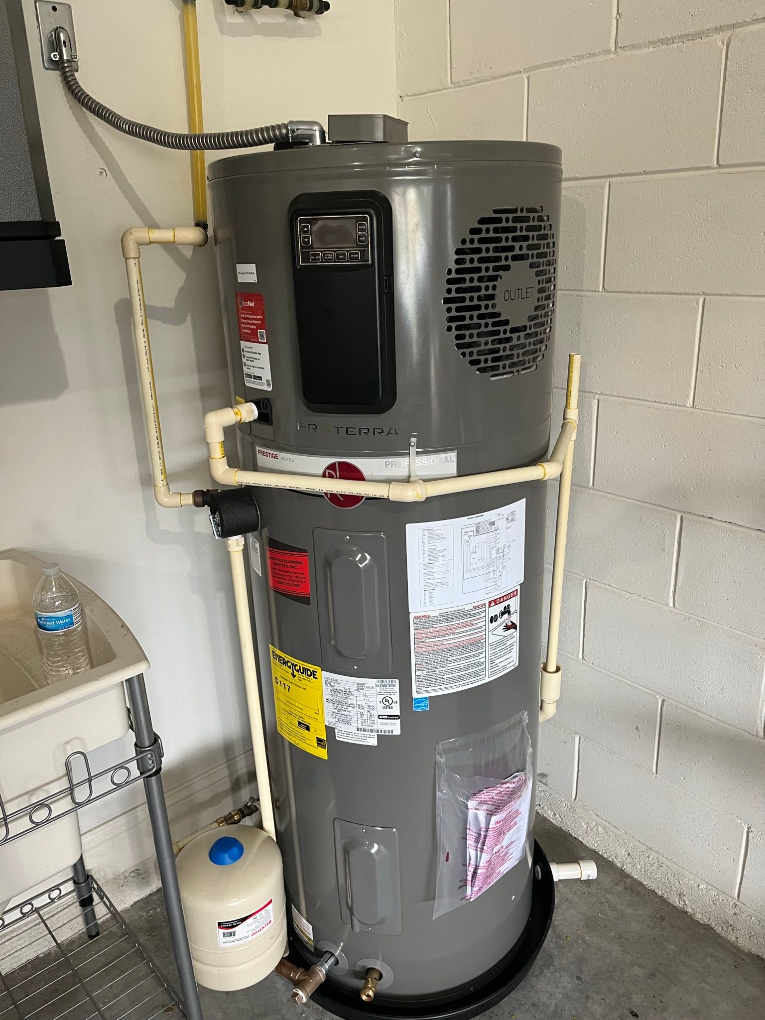 Large gray water heater tank mounted indoors near the ceiling, with a yellow energy label.