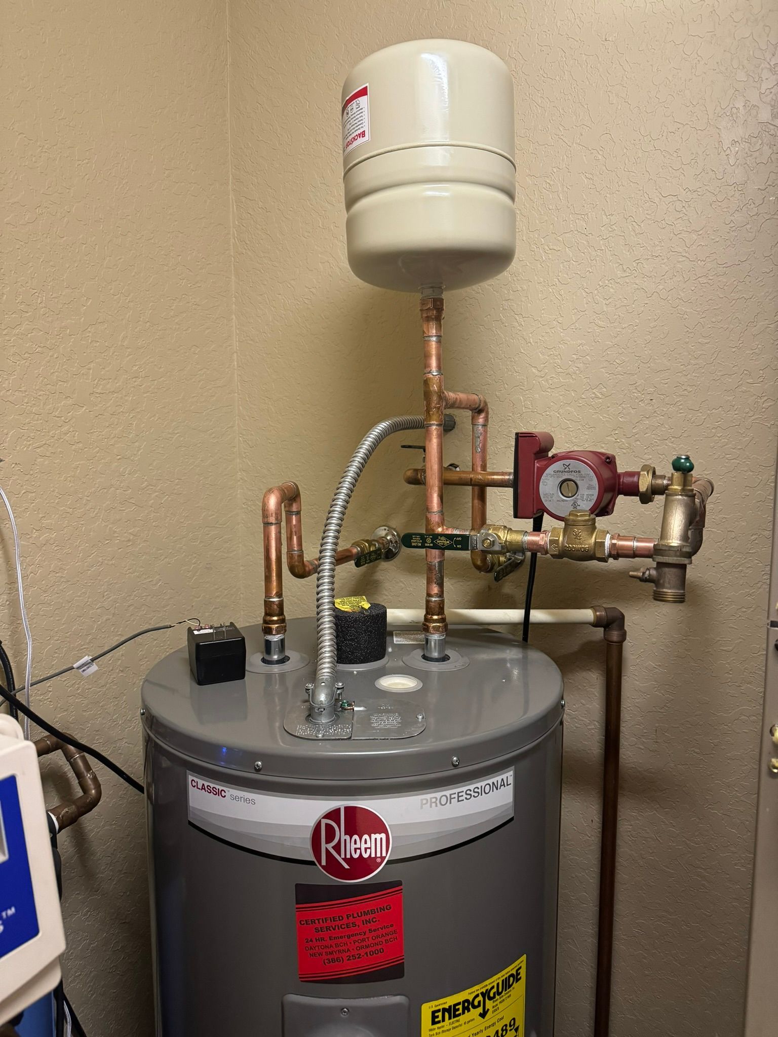Water heater and utility equipment in a small mechanical room with pipes, tanks, and gauges