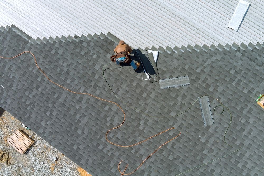 Person standing on a gray shingled roof near a white wall, with ropes coiled around them.