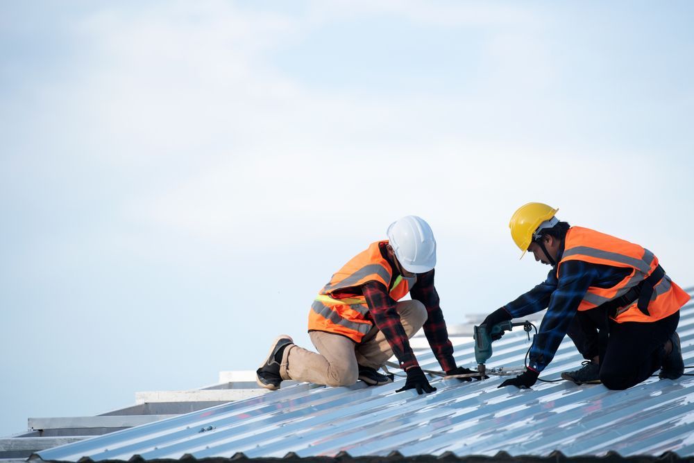 Two construction workers in hard hats installing roofing panels on a metal roof.