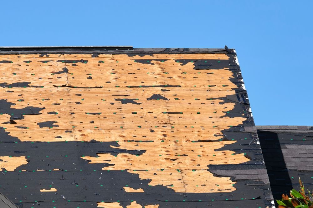Peeling tan paint on a dark roof under a clear blue sky