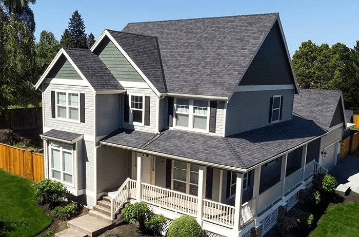 Aerial view of a gray two-story suburban house with a wraparound porch and dark shingled roof.