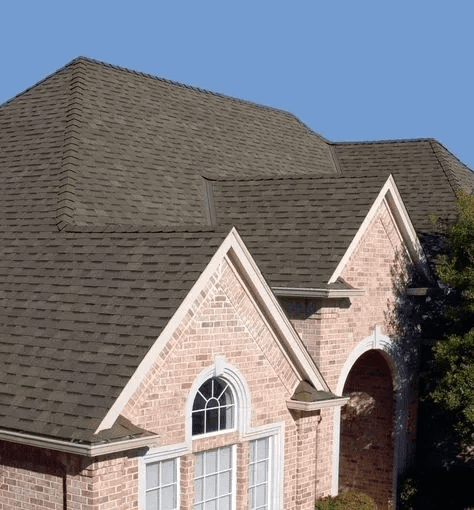 Brick house exterior with steep gray shingle roof and arched windows under a blue sky