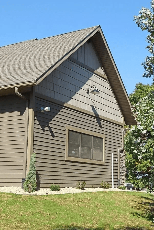 Side view of a gray house with tan siding, a gabled roof, and grassy yard under a blue sky