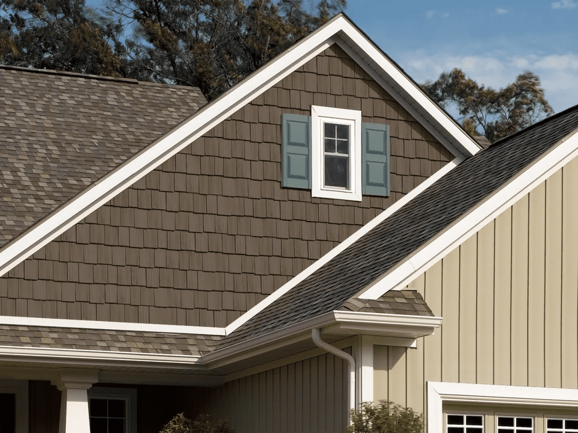 Residential house roof with brown shingles and a small dormer window with blue shutters