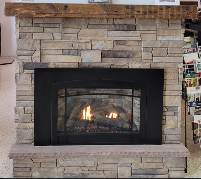 A man is putting logs in a firewood basket in front of a fireplace.